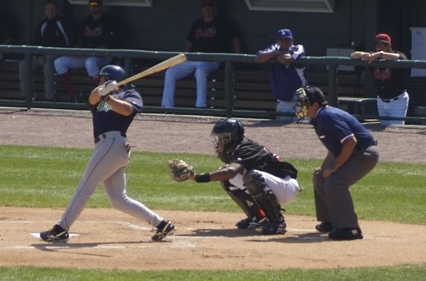 A batter mid-swing at home plate with a catcher crouching behind.