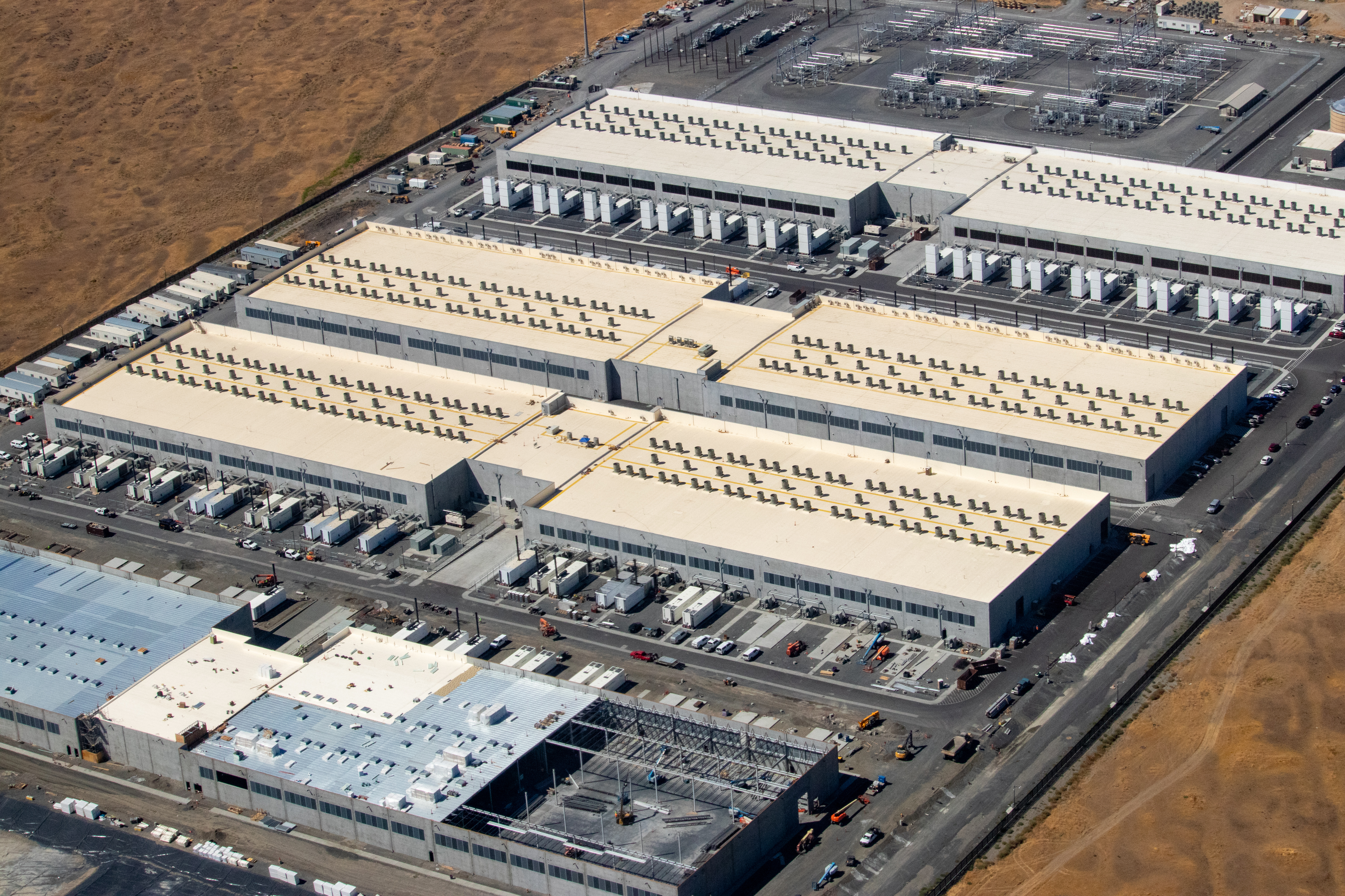 Aerial view of several large rectangular data center buildings with rooftop cooling units.
