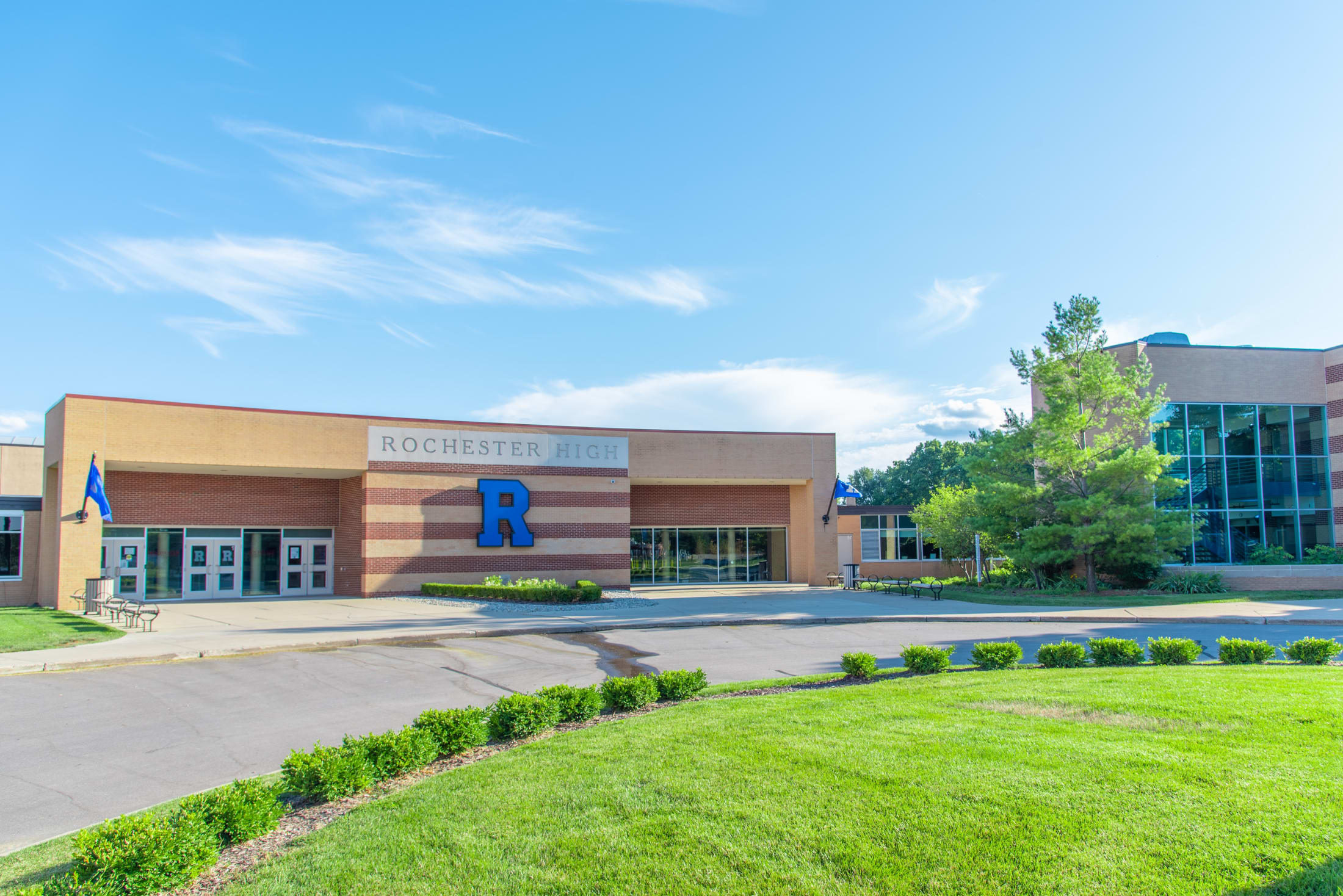 Main entrance of a brick high school building with a blue R logo and school name sign.