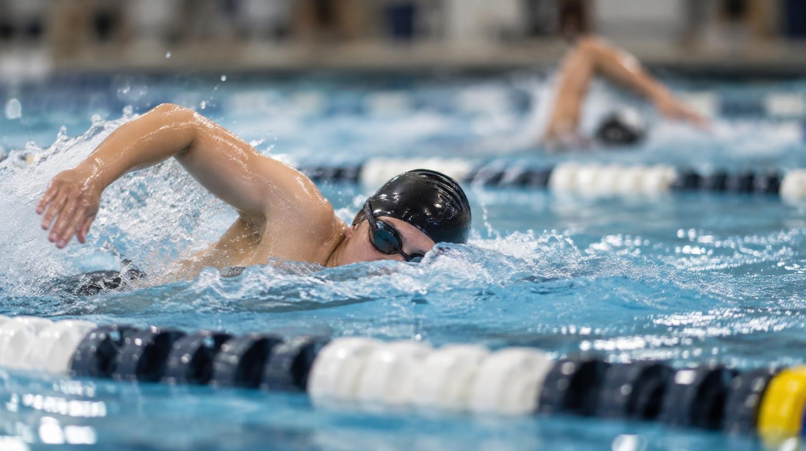 Swimmer mid-stroke in a pool lane wearing a cap and goggles, water splashing.