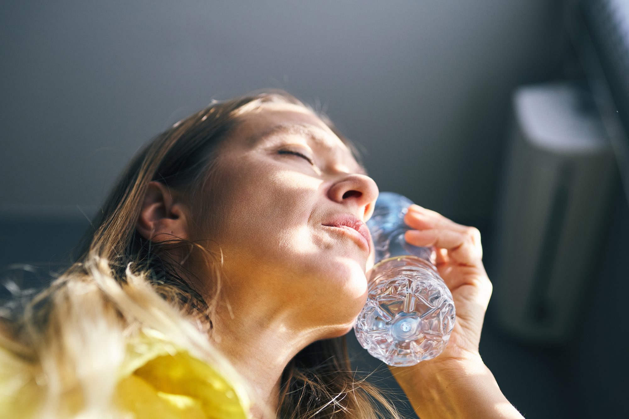 Woman suffering from a heatwave cooling her flushed neck with a cold water bottle indoors