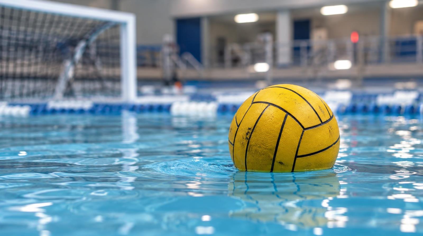A water polo ball floating on the surface of a bright blue pool with a goal net in the background.