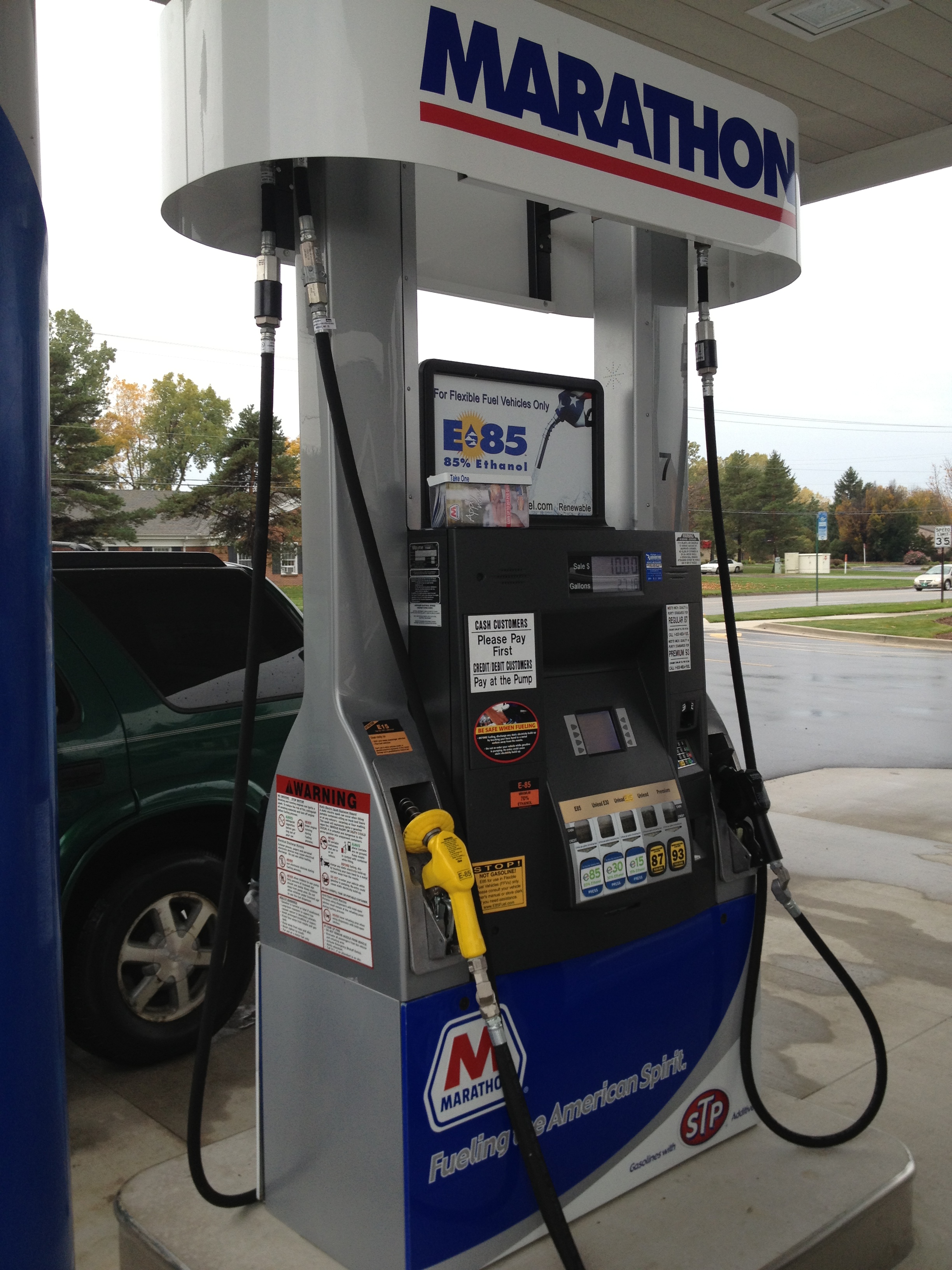 Marathon-branded fuel pump with yellow flex-fuel nozzle at a gas station.