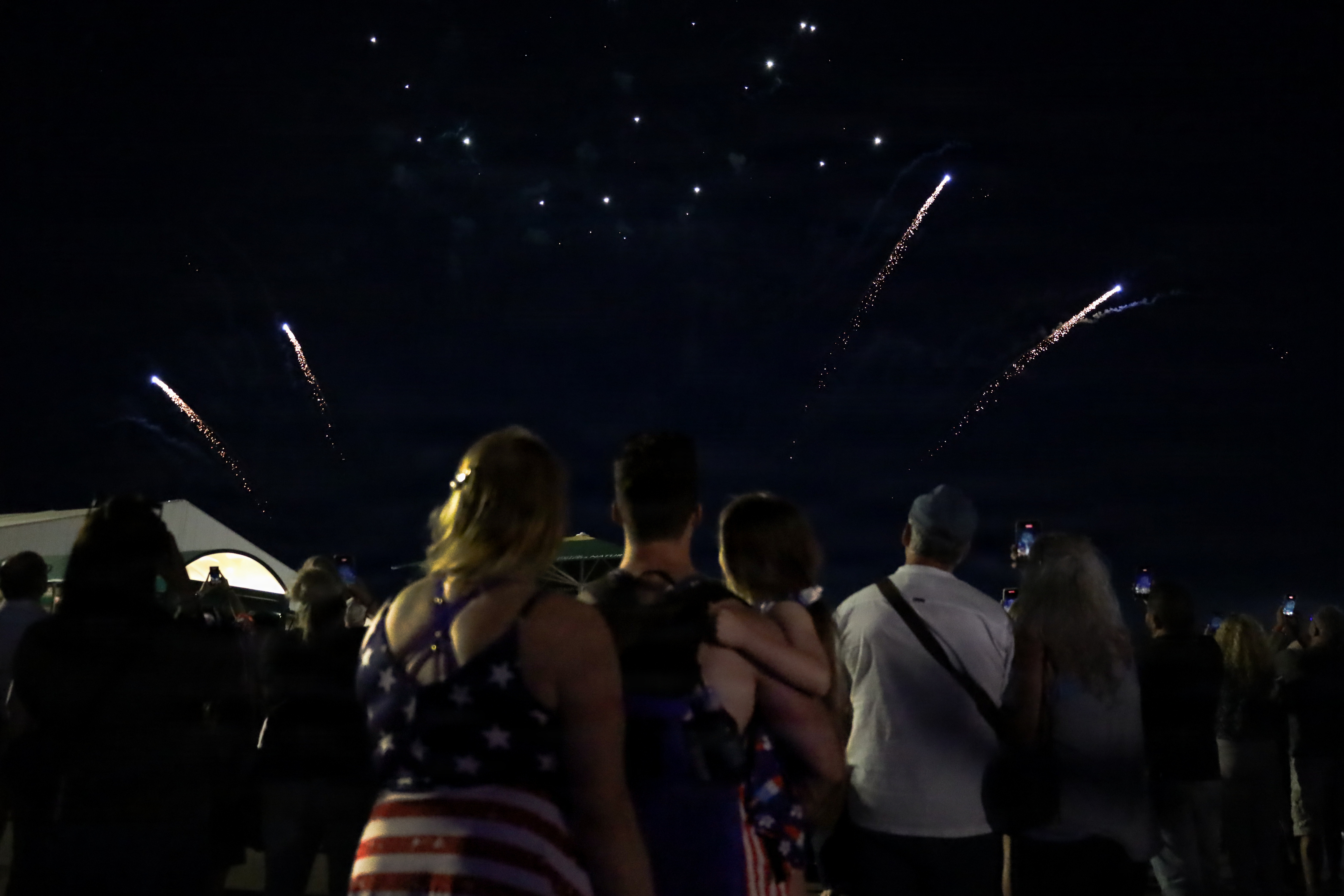 A crowd of people watches colorful fireworks burst in a dark night sky.