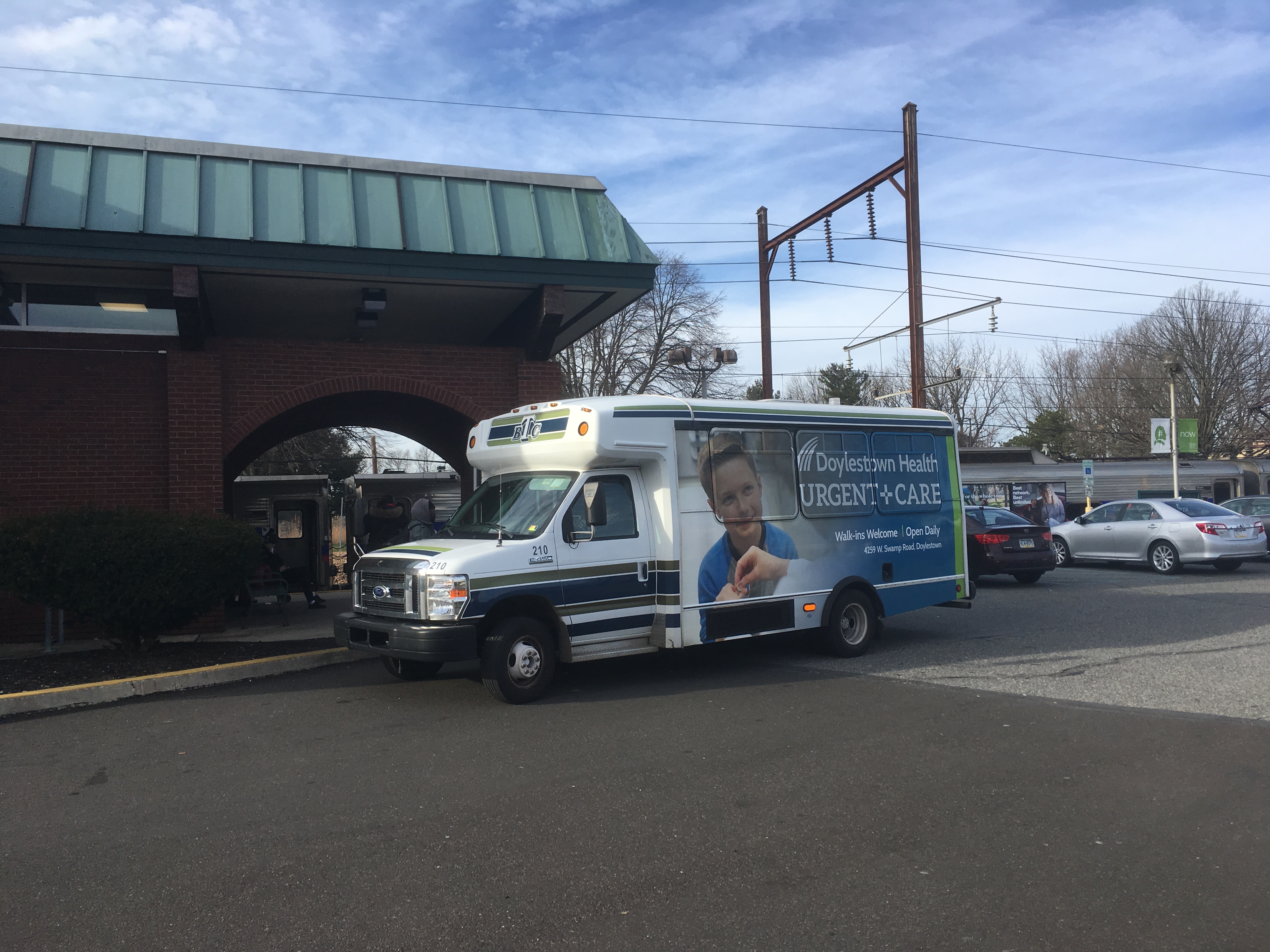 A small Bucks County Transport bus parked in a lot near a brick building.