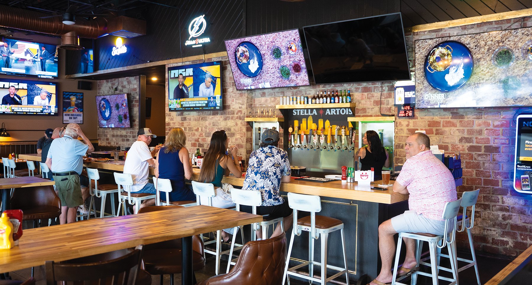 Patrons seated at a pub bar counter with beer taps and flat-screen TVs.