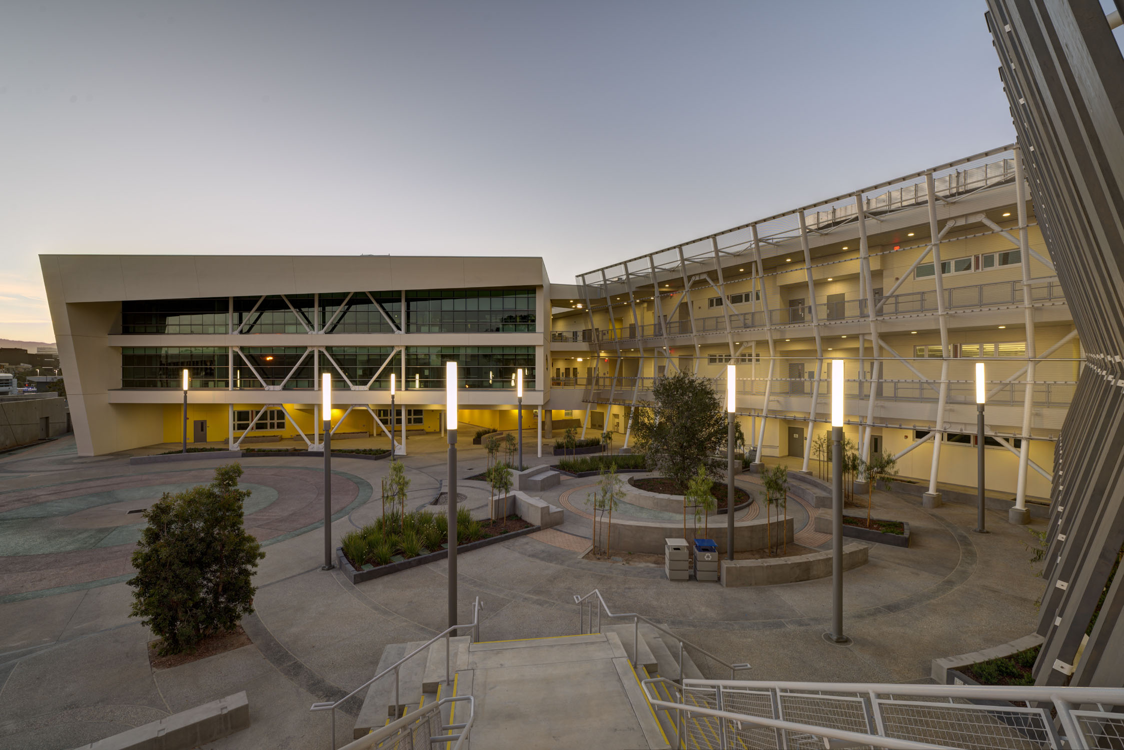 Modern multi-story school building with open courtyard and illuminated columns photographed at dusk.
