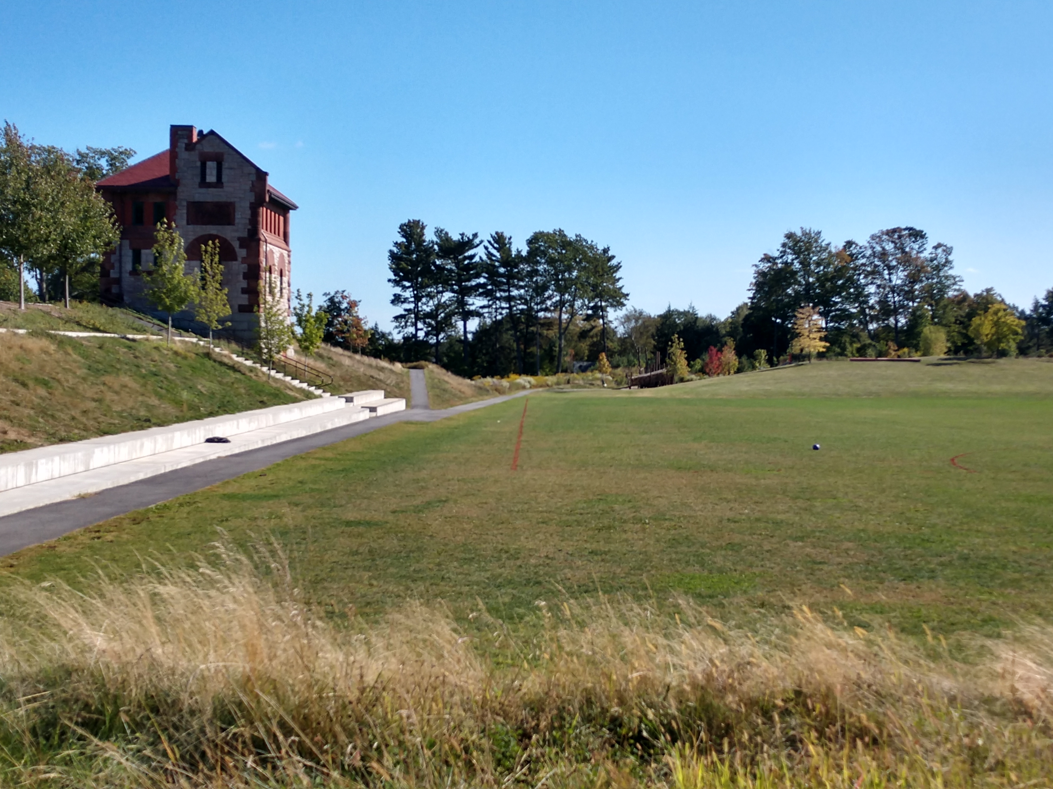 A manicured green sports field with a stone building on a hill and trees in the background.