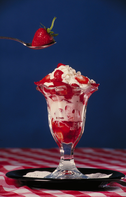 A strawberry sundae in a glass dish topped with whipped cream and fresh strawberries.