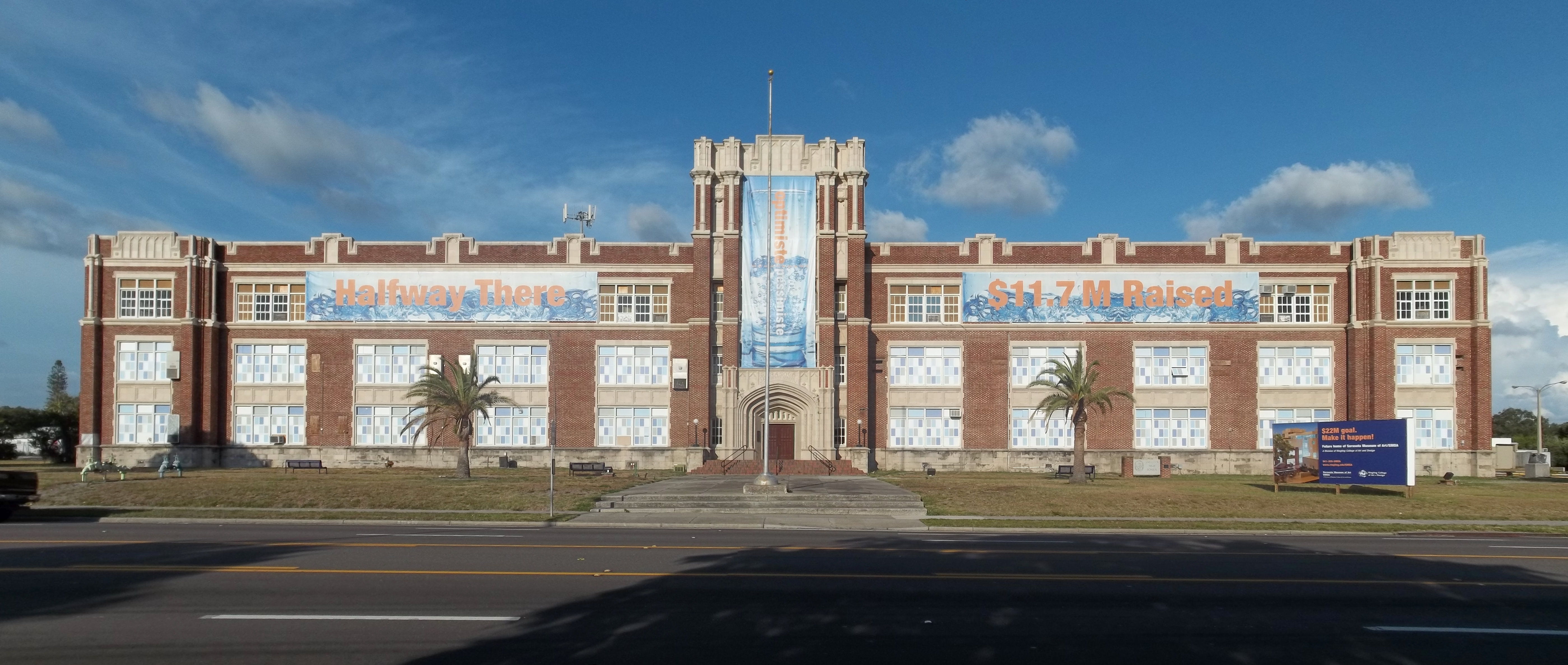 Red-brick Art Deco high school building with palm trees flanking the main entrance.