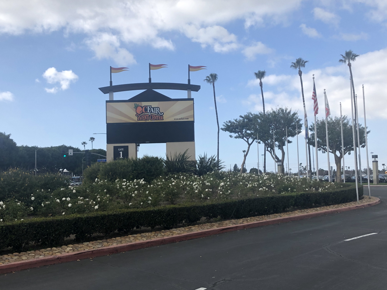 Entrance marquee sign for the OC Fair and Event Center with palm trees and flags.