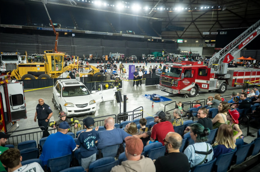 Arena floor with a red fire truck, construction equipment, and spectators in stadium seating.