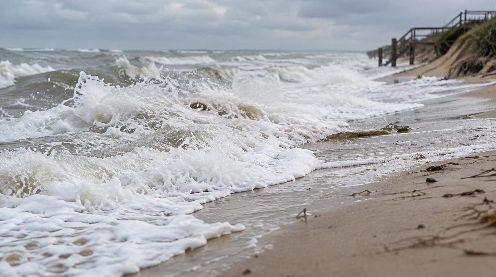 Ocean waves washing far up a sandy beach shoreline under overcast skies.