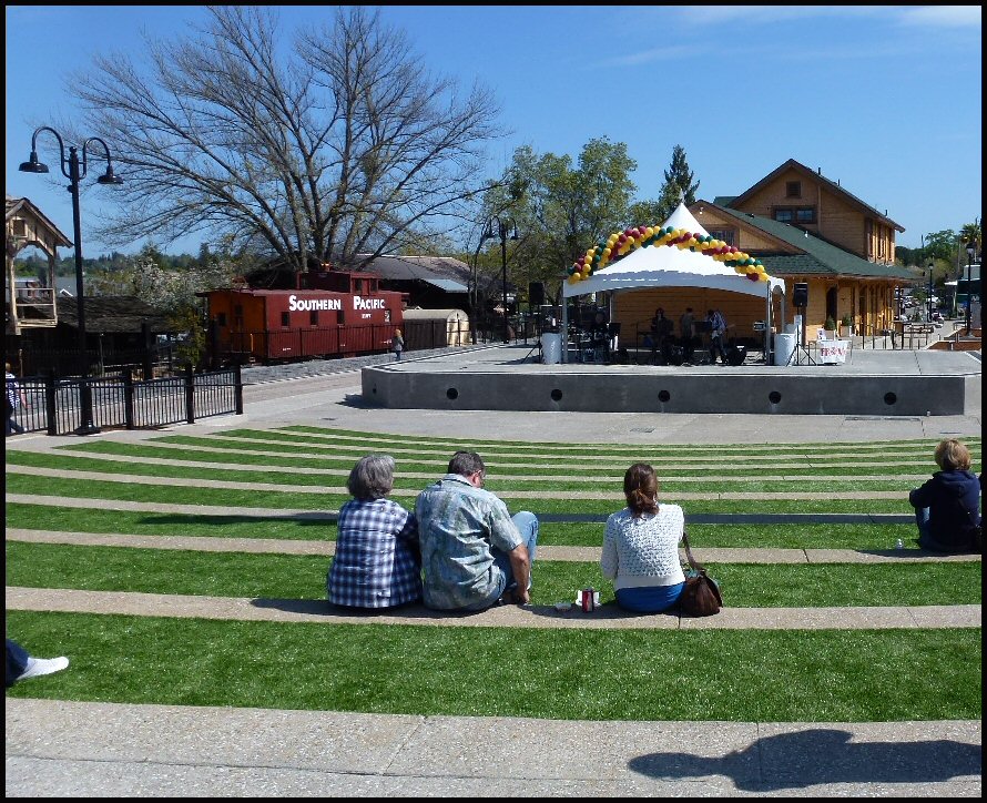 Outdoor amphitheater with grass seating terraces and a white tent-covered stage.