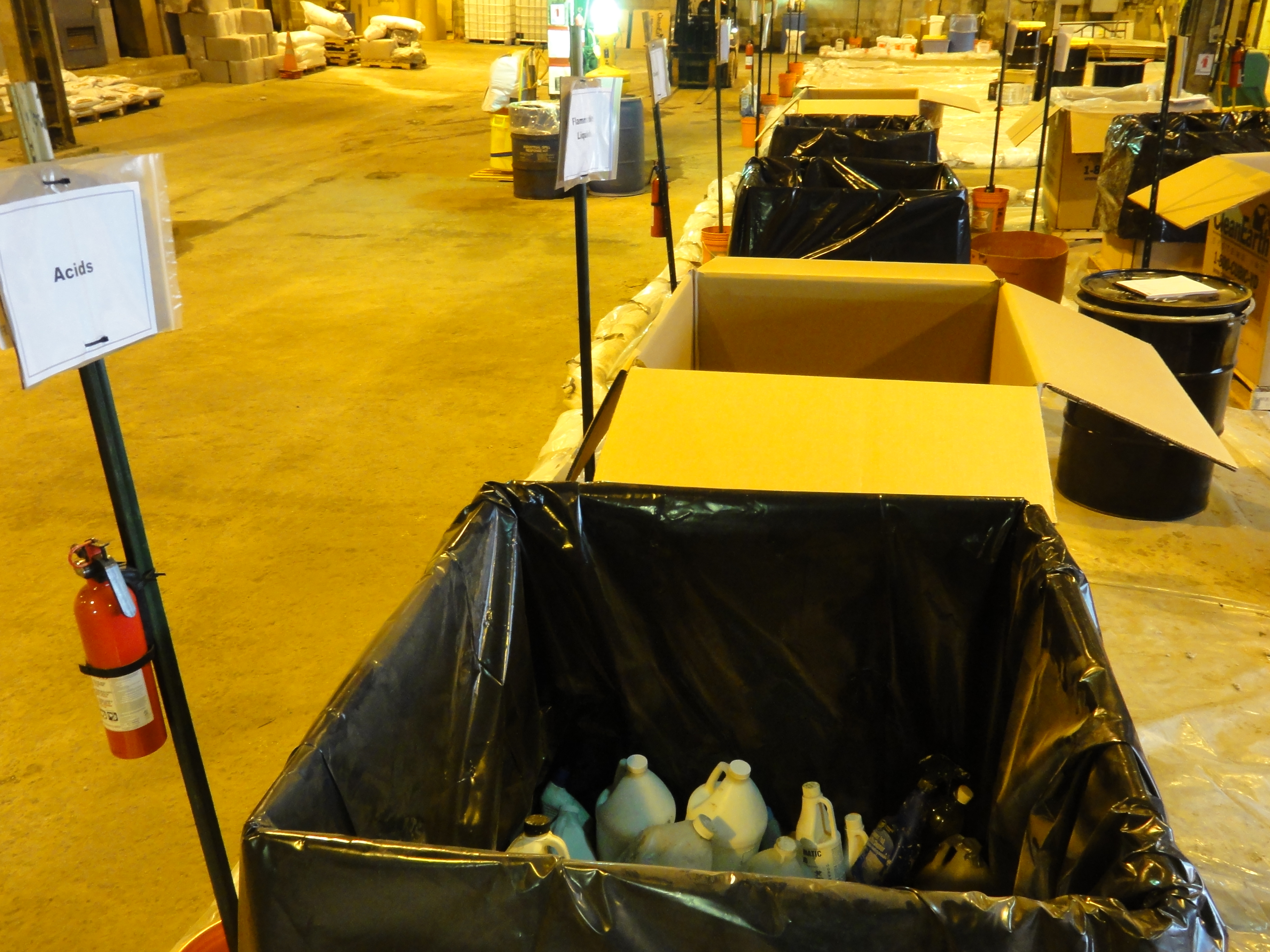 Rows of labeled collection bins inside a large indoor waste sorting facility.