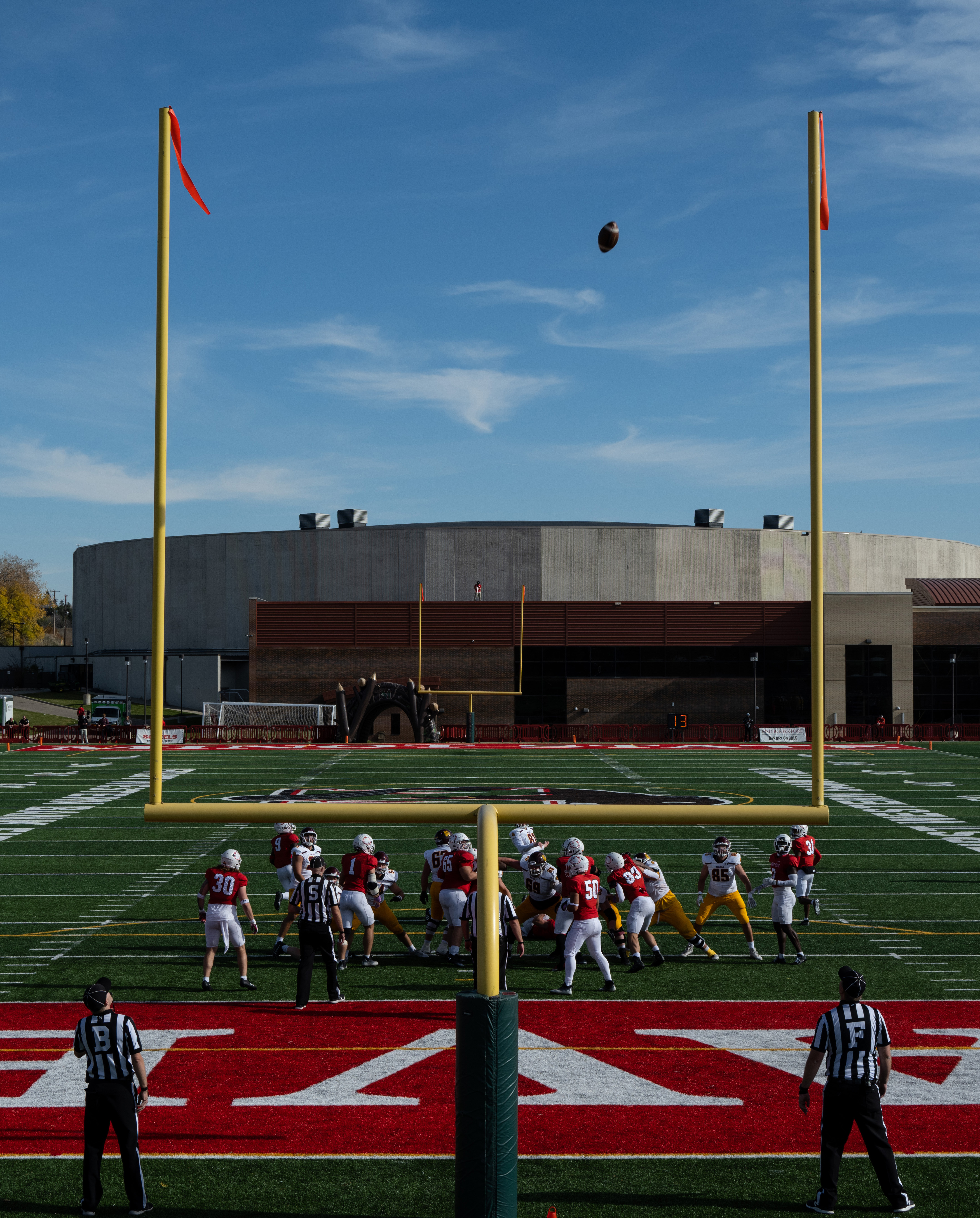 Football players on a field during a game, with yellow goalposts in the foreground.