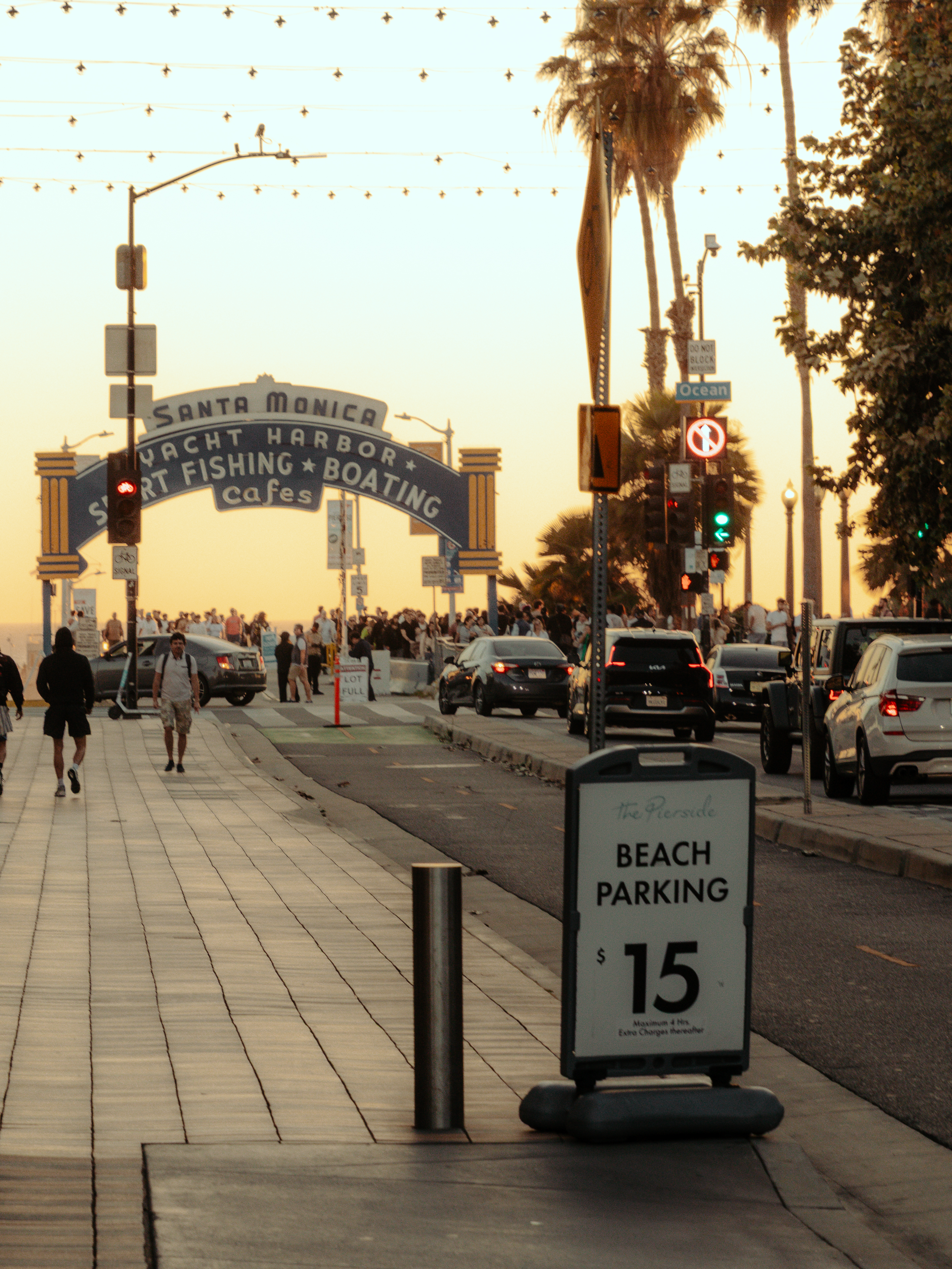 Santa Monica Pier entrance arch sign with palm trees and string lights at golden hour.