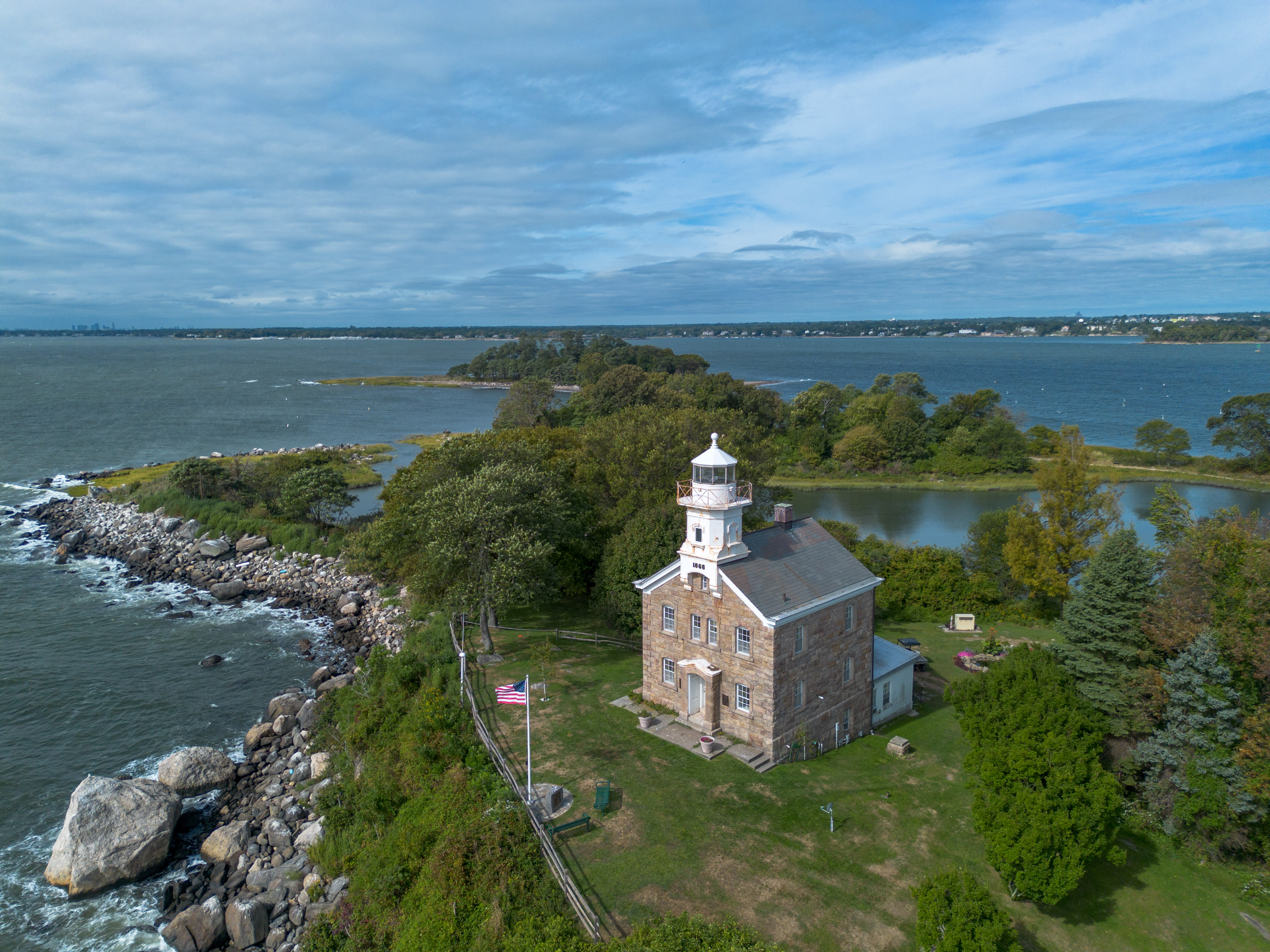 Aerial view of a stone lighthouse on a small wooded island surrounded by water.