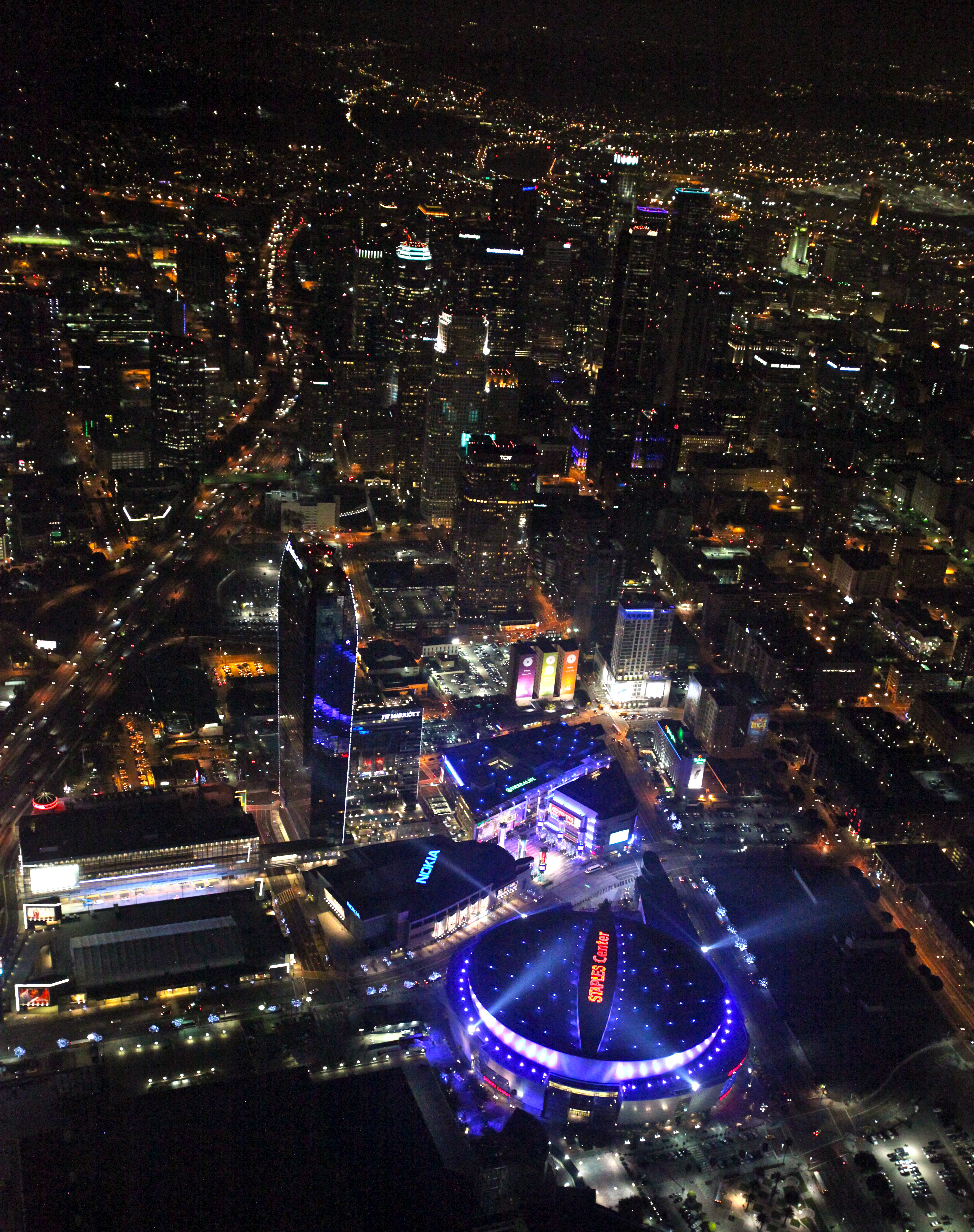Aerial nighttime view of a large illuminated arena surrounded by city lights.