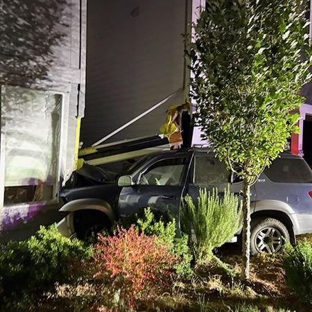 An SUV crashed into the exterior wall of a multi-story building at night, with structural damage visible.