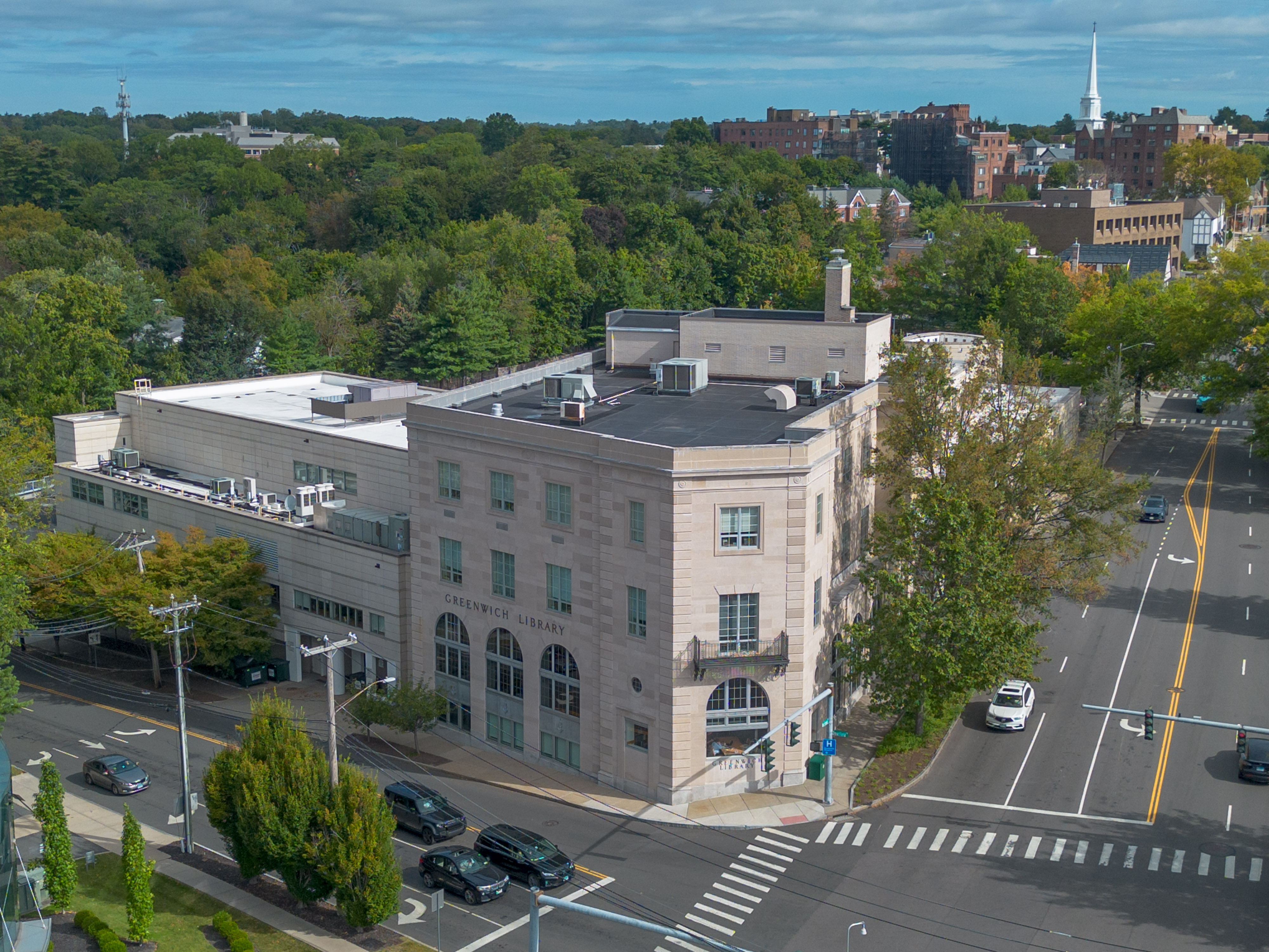 Aerial view of a large stone library building at a street intersection surrounded by trees.