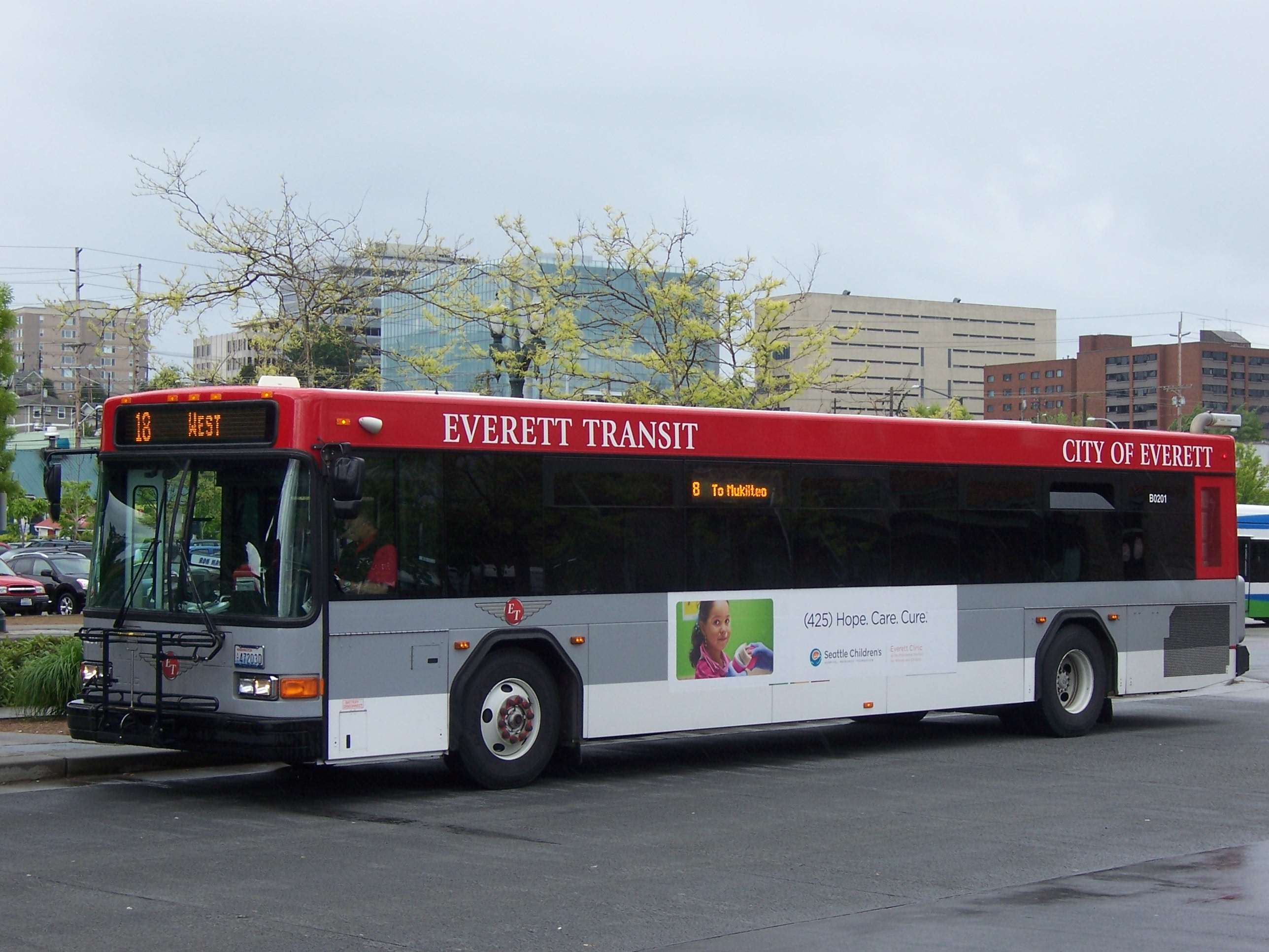 A red and gray Everett Transit bus at a transit station with city buildings behind it.