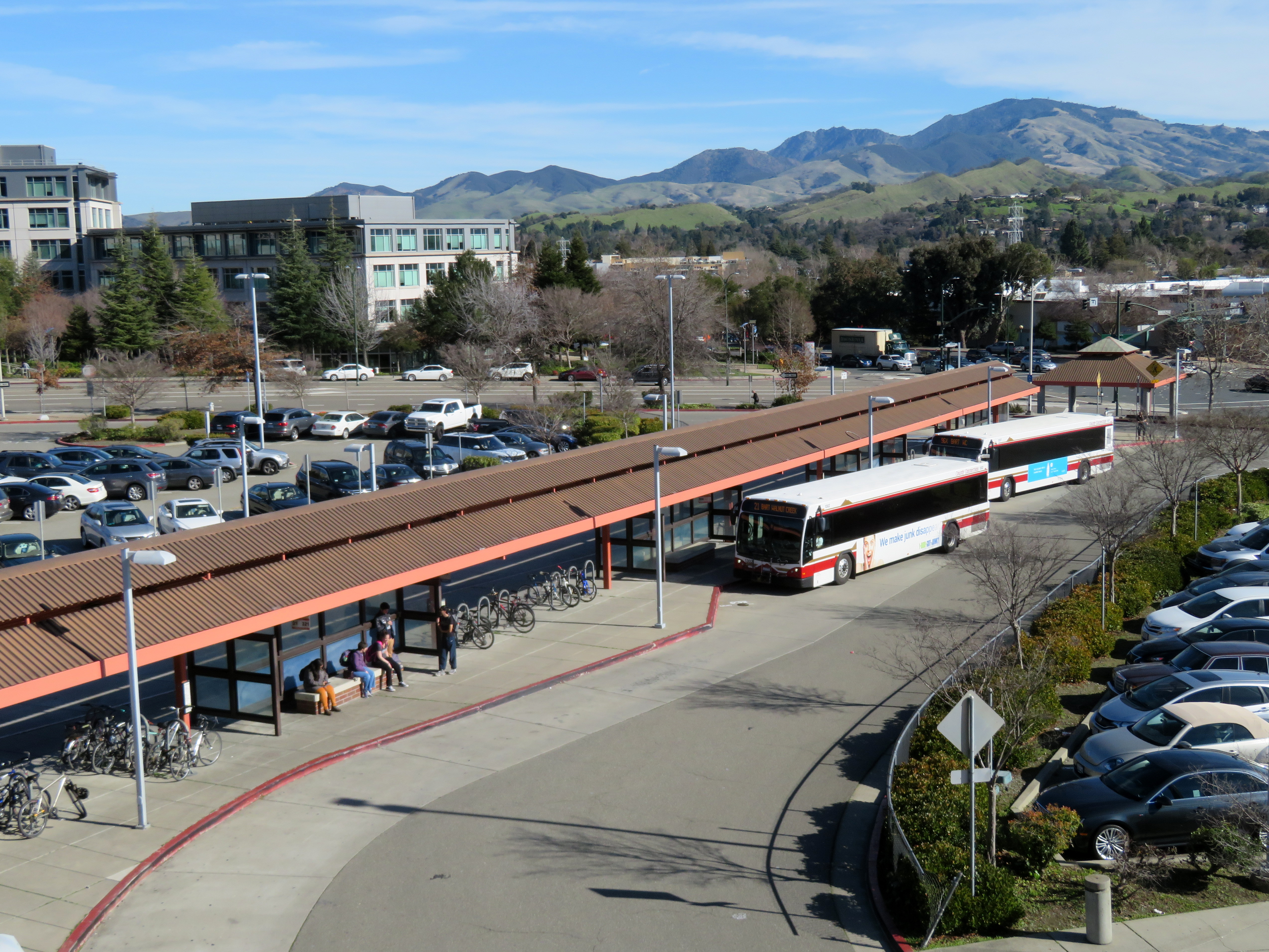 Elevated view of a bus transit station with covered platforms, parked buses, and mountains in the background.