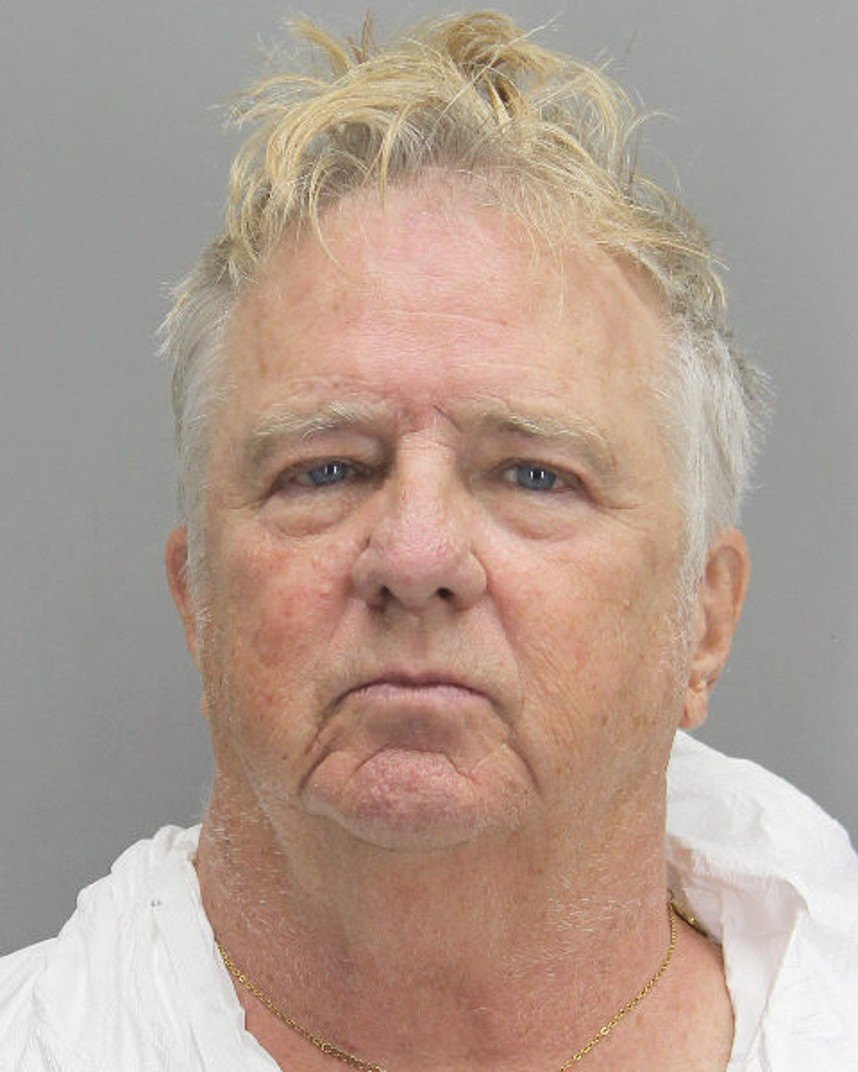 Mugshot of an older man with disheveled blonde hair wearing a white shirt and gold chain.