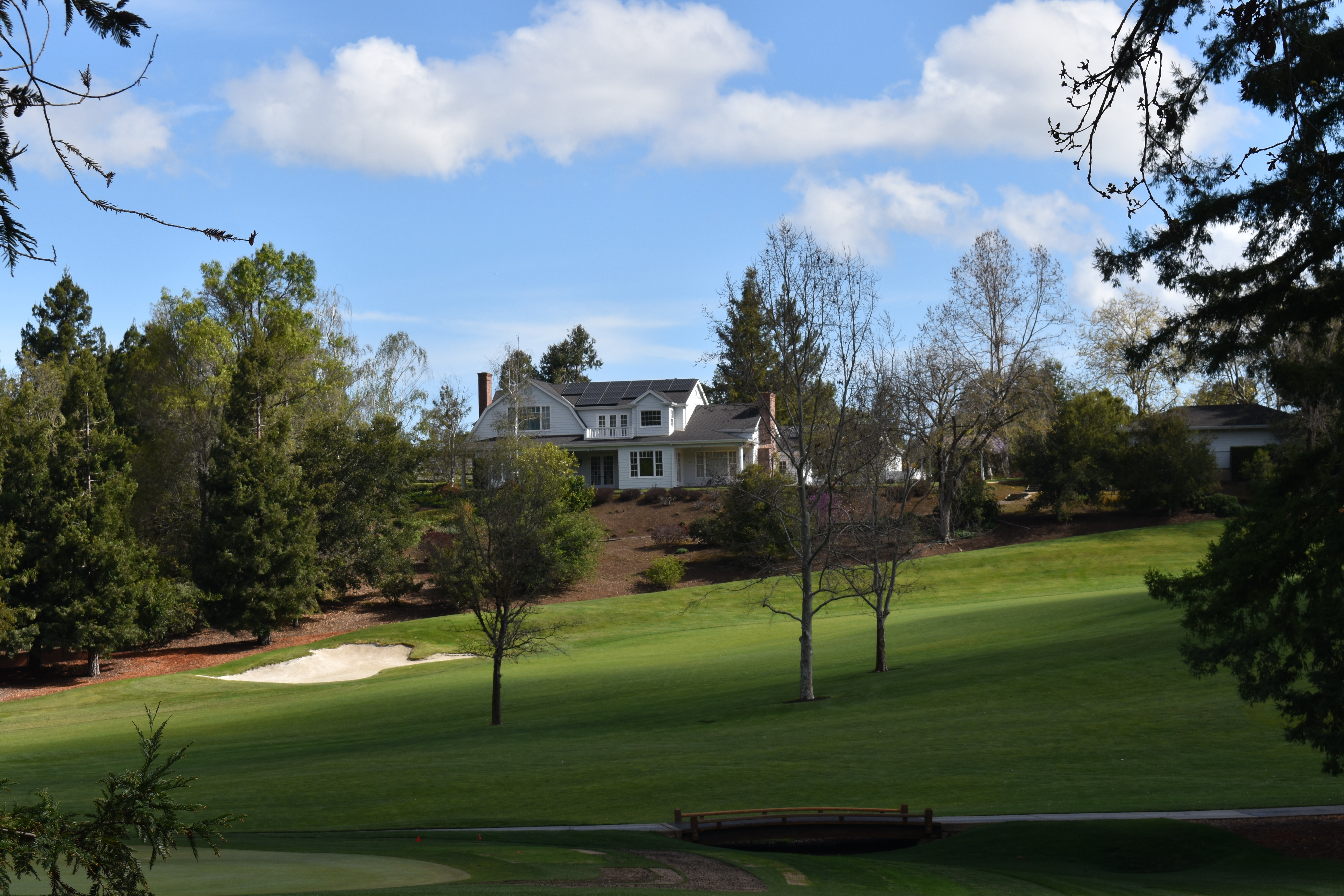 Manicured golf fairway with sand bunker, small bridge, and white clubhouse in background.