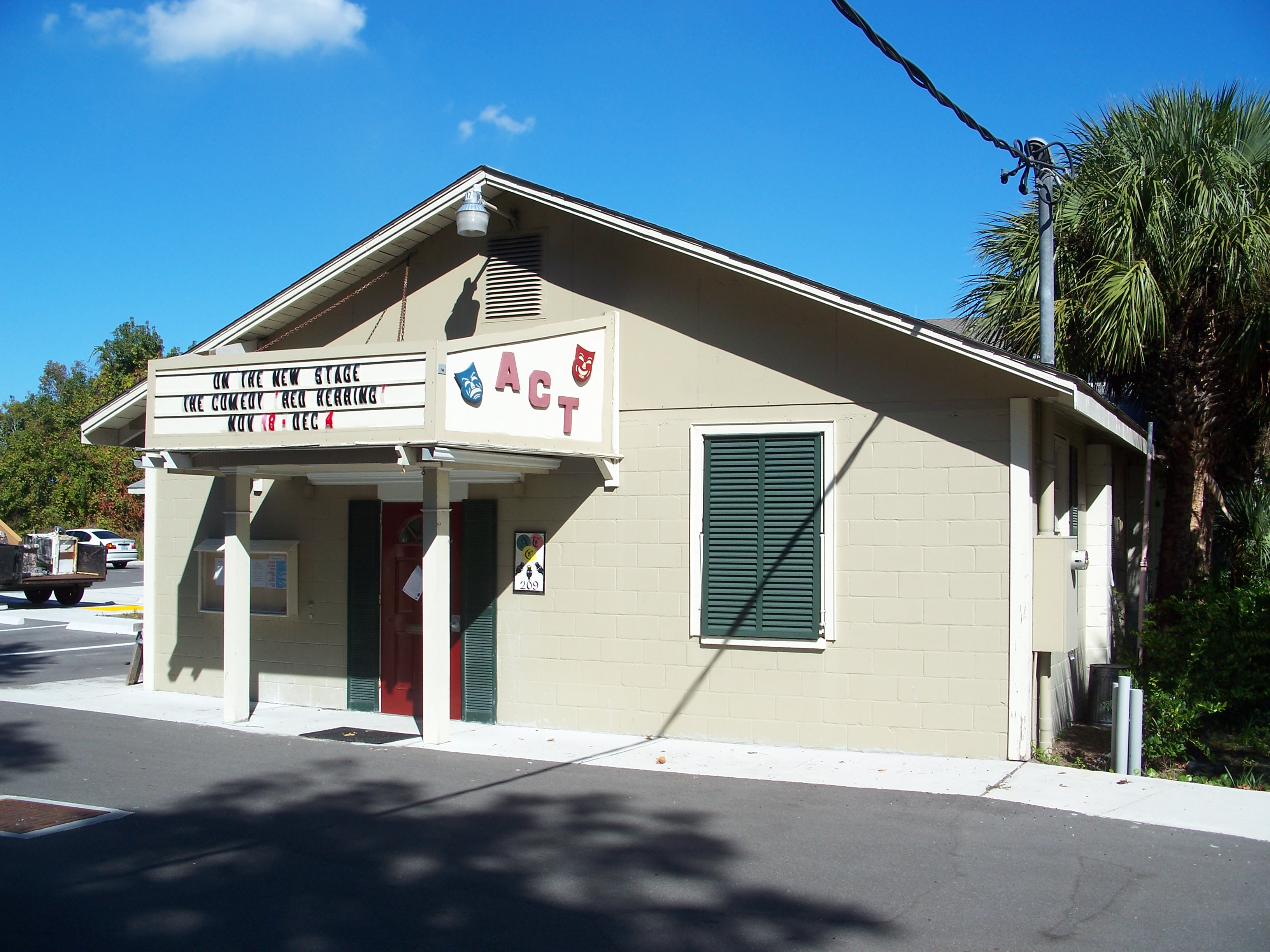 Small theater building with a marquee sign, red door, and green shutters.
