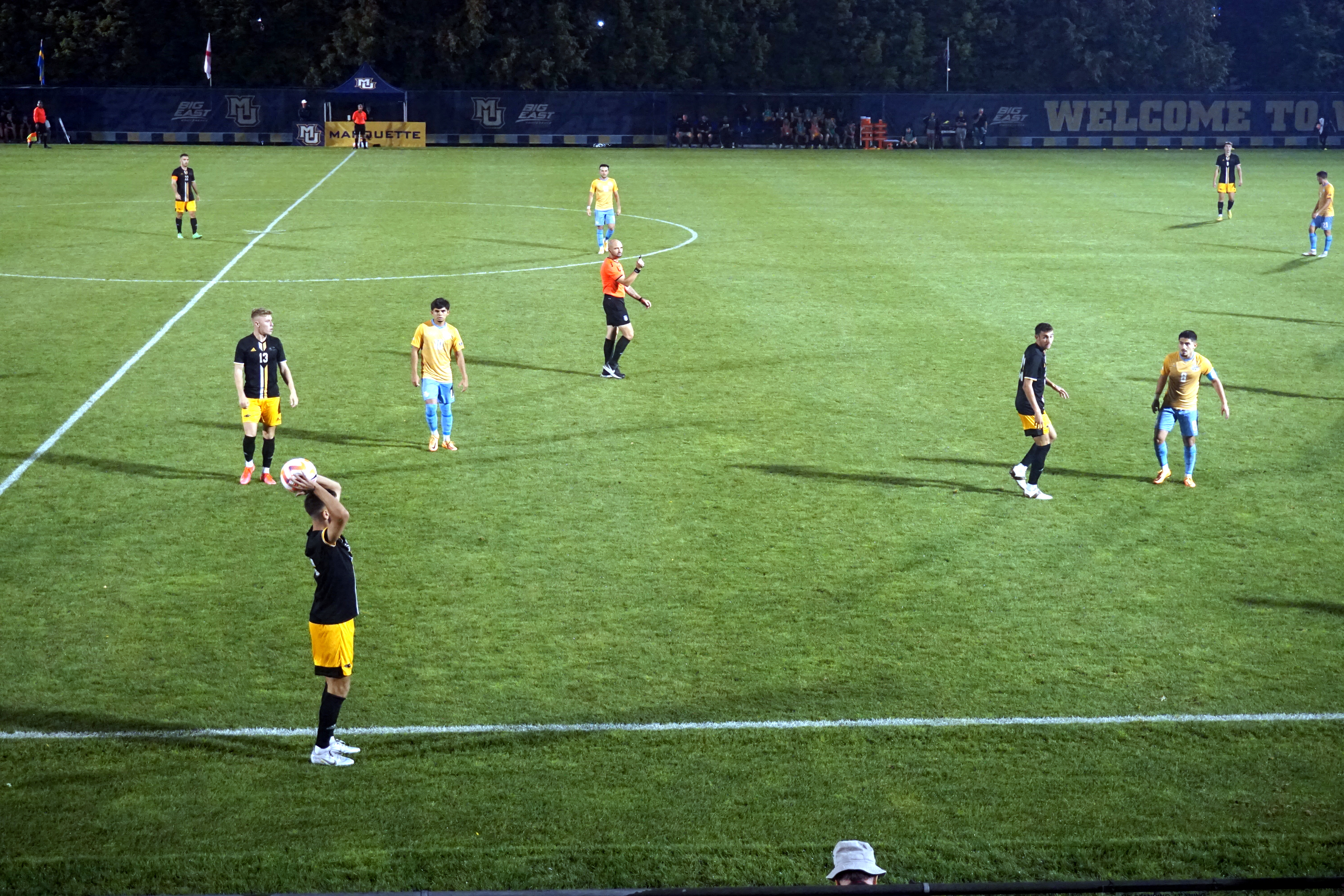 A player takes a throw-in during a nighttime soccer match under stadium lights.