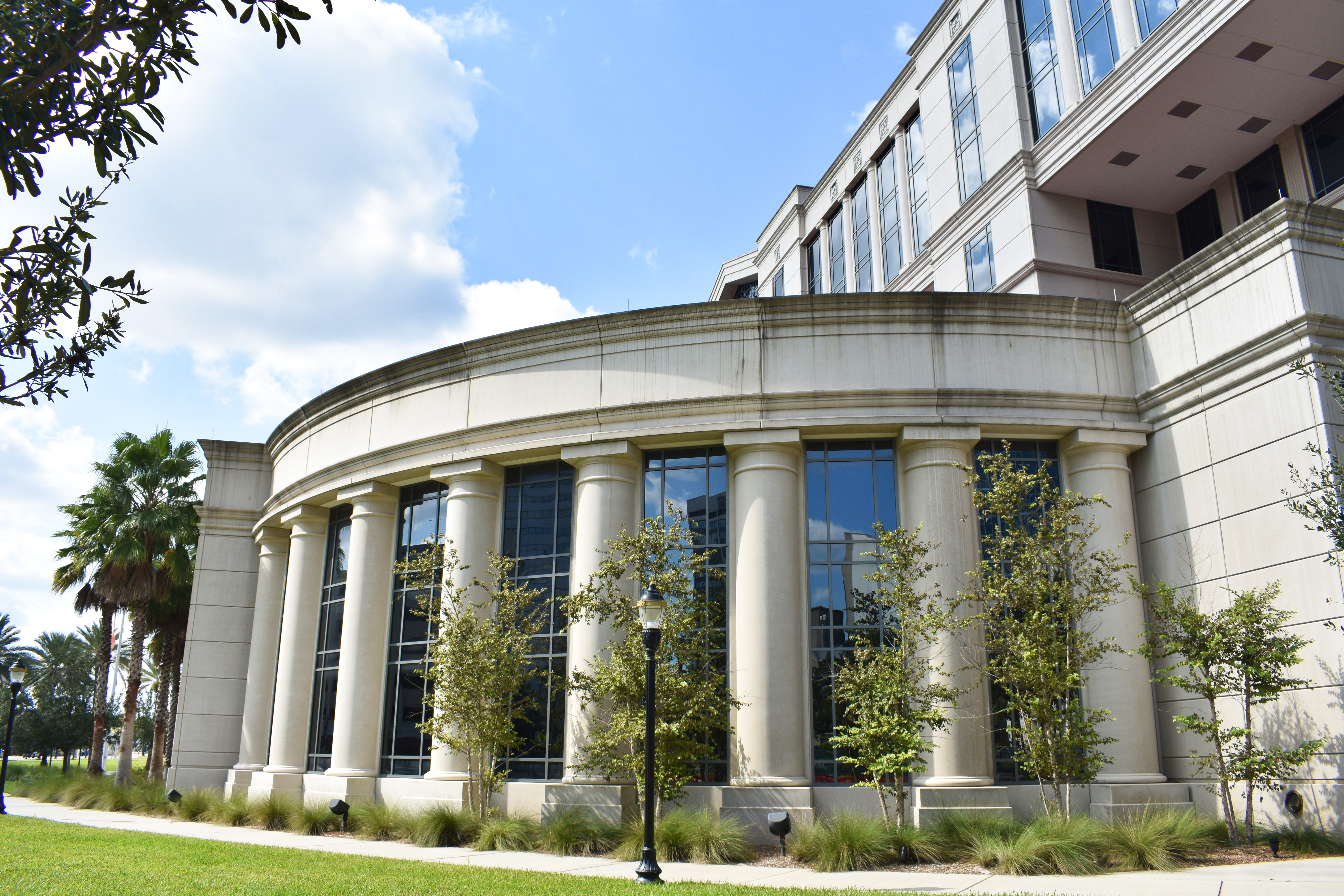 Government building with tall stone columns, glass windows, and palm trees.