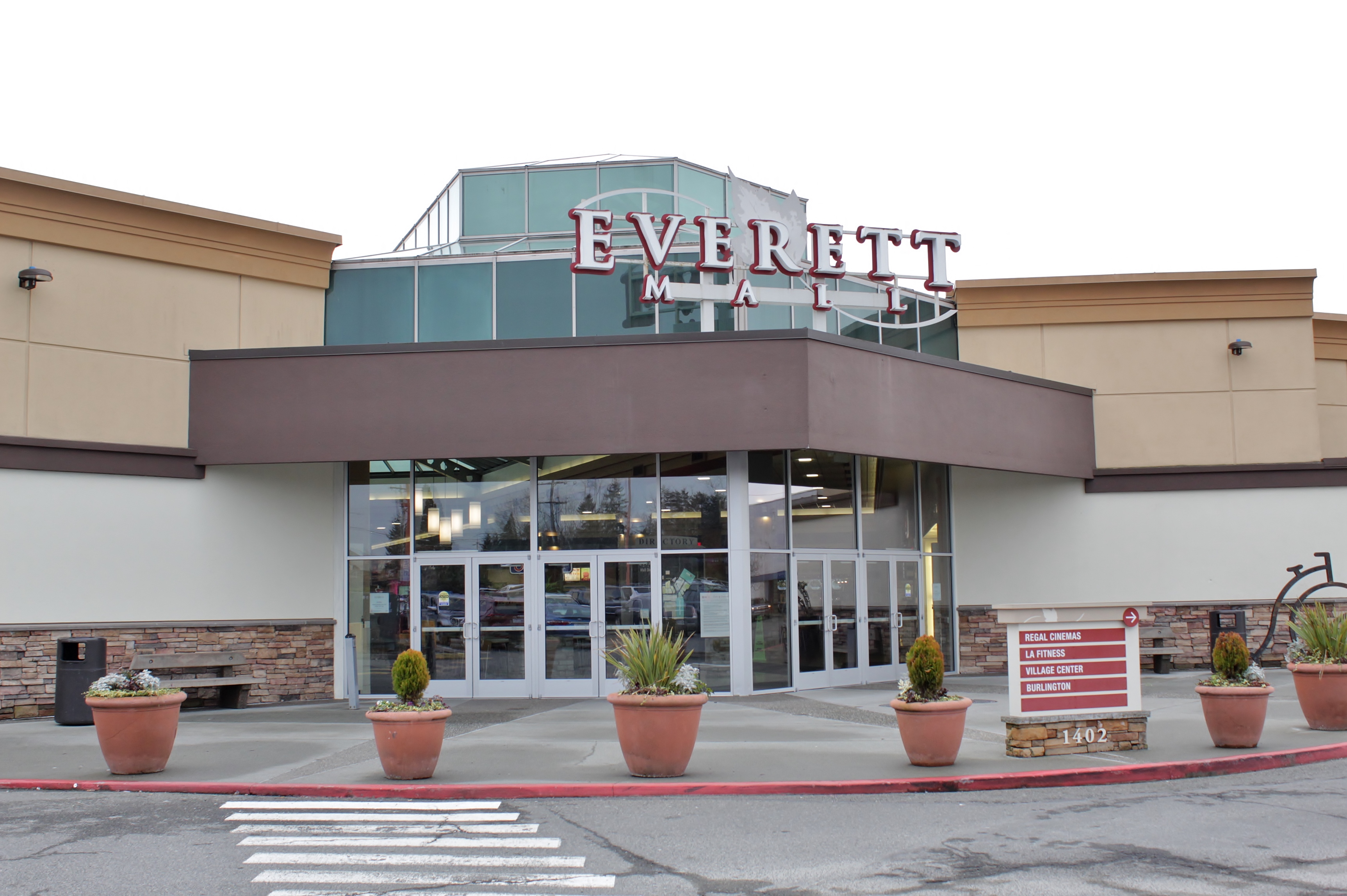 Front entrance of a shopping mall with signage above glass doors and a parking lot.