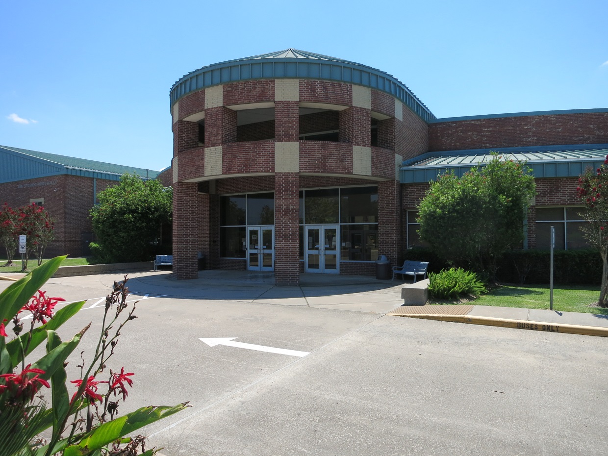 Exterior of a brick school building with a rounded entrance tower under a clear blue sky.