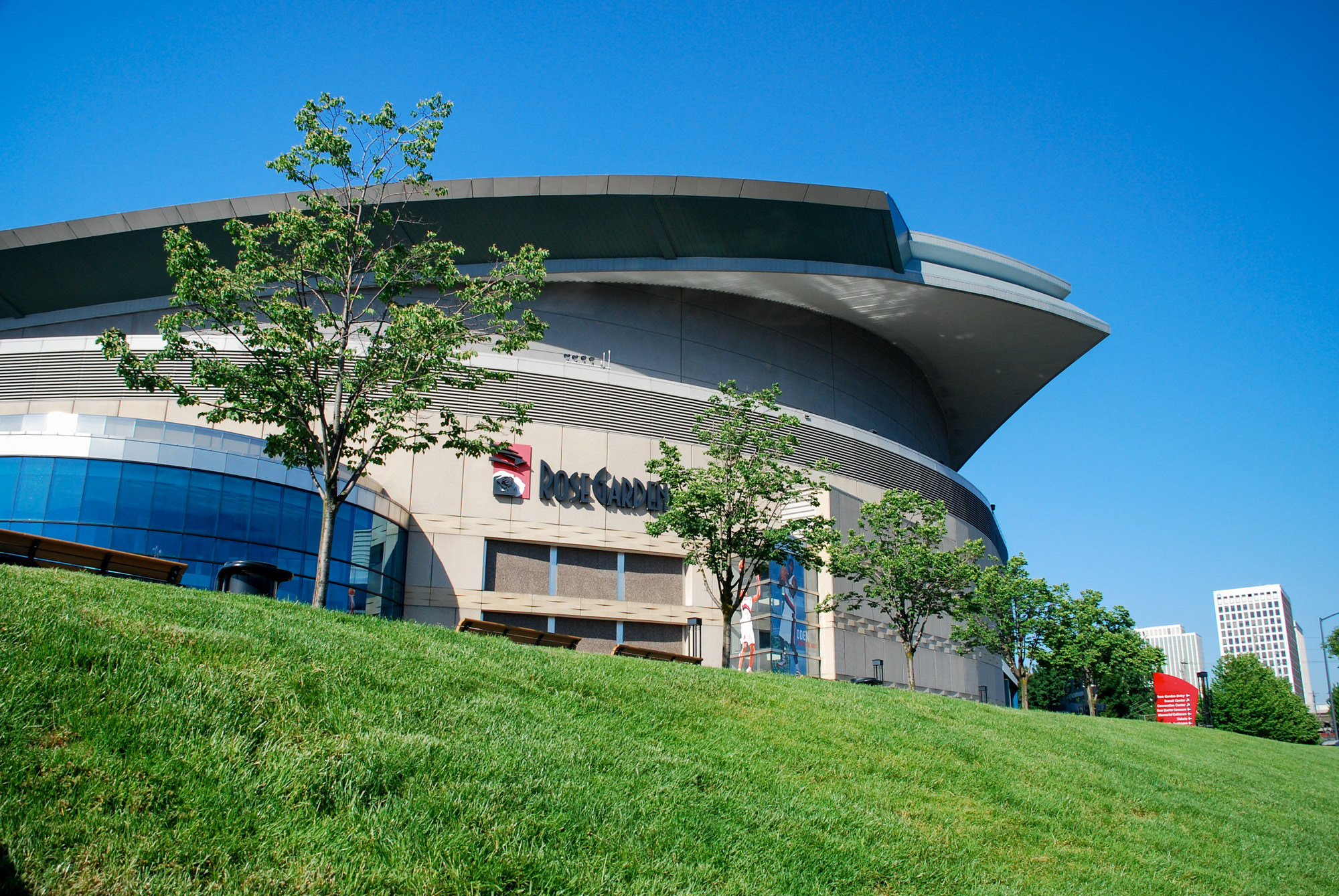 Large curved arena building with green lawn and trees in the foreground.