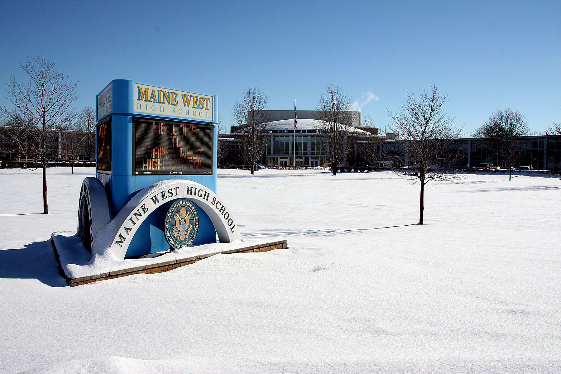 Maine West High School sign and building exterior in winter with snow on the ground.