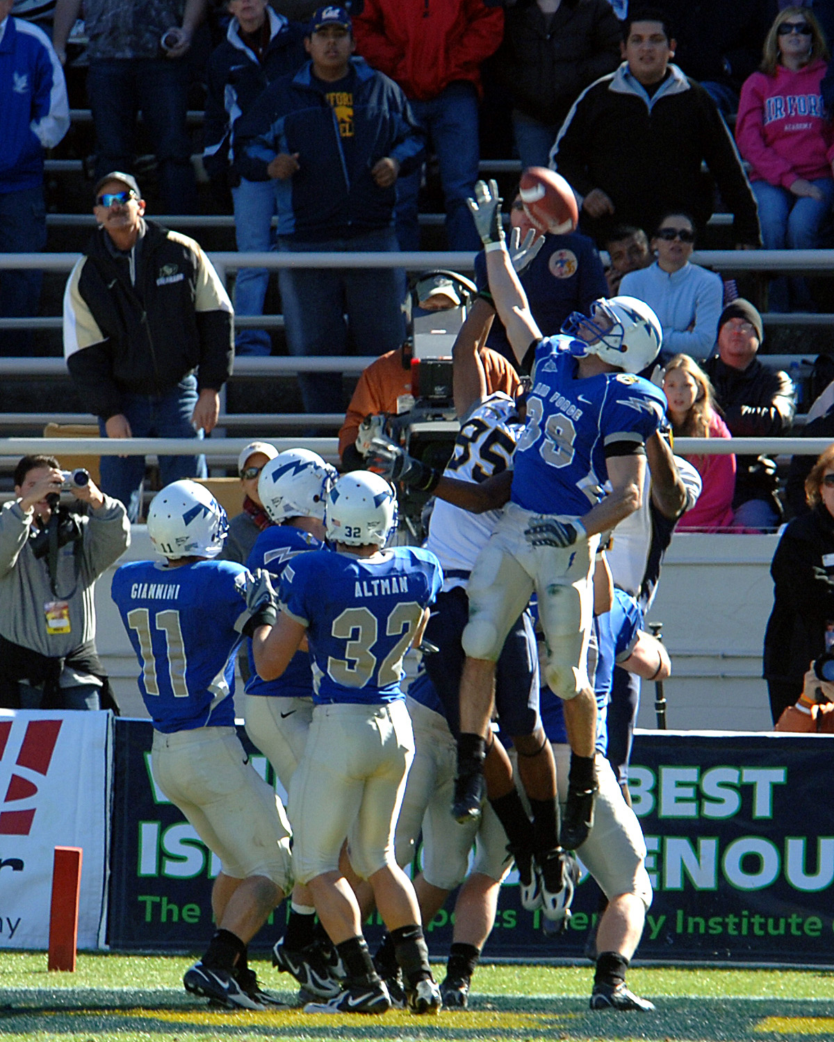 Football player in blue uniform leaps to defend a pass near the end zone.