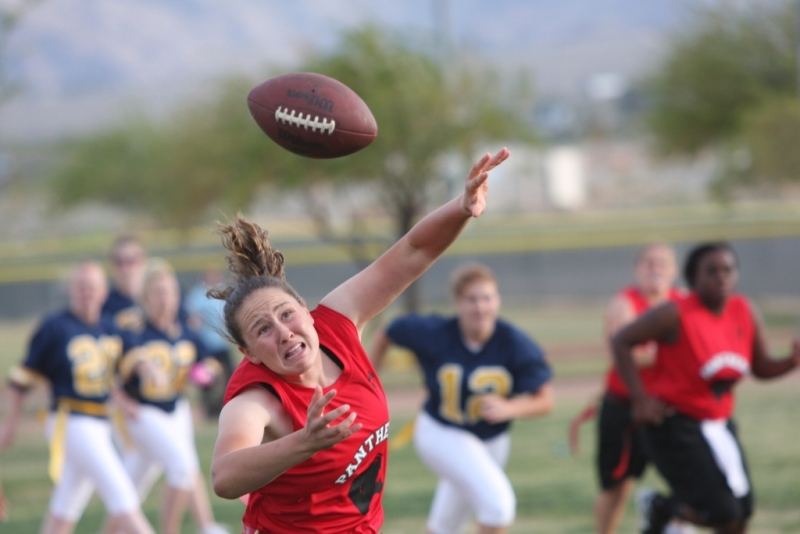 A woman in a red jersey throws a football on a grass field.