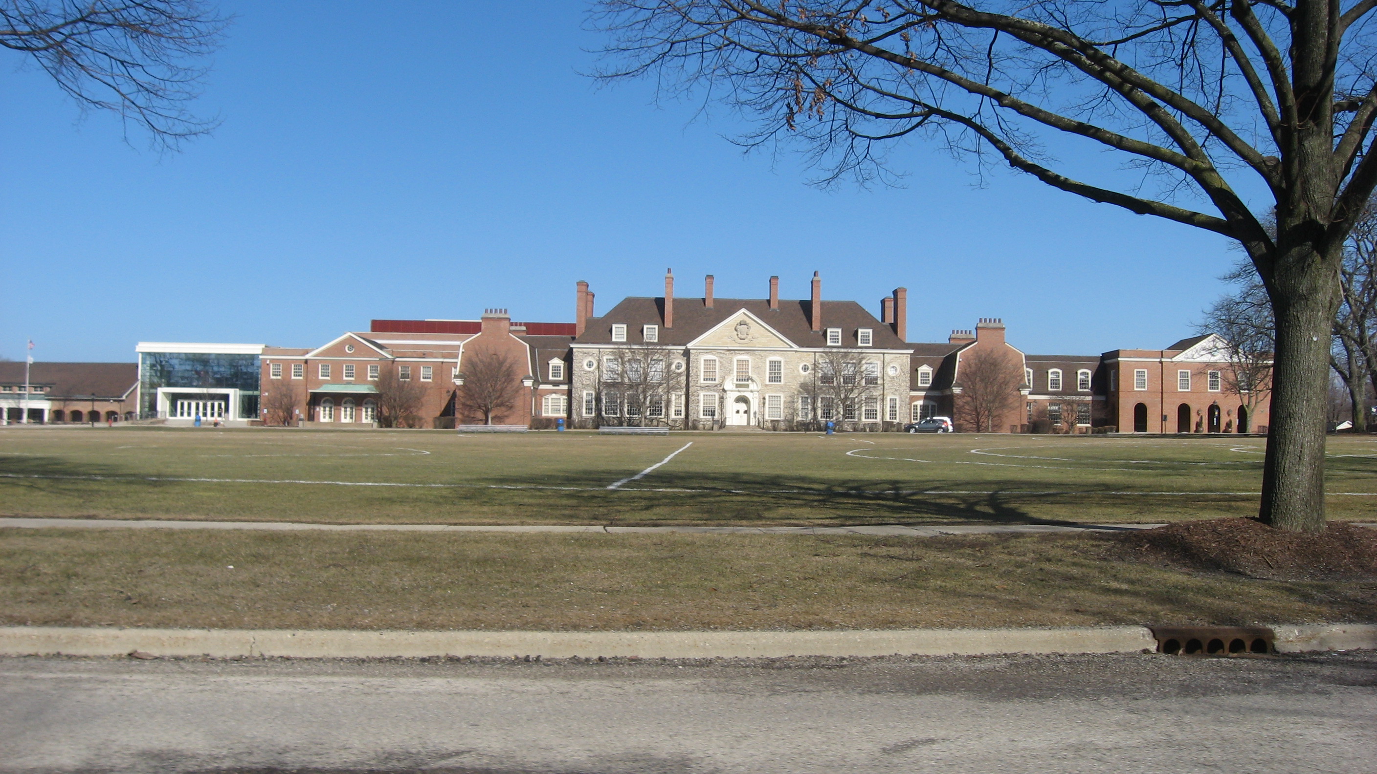 Front facade of a large red brick high school building across a wide lawn with bare trees.