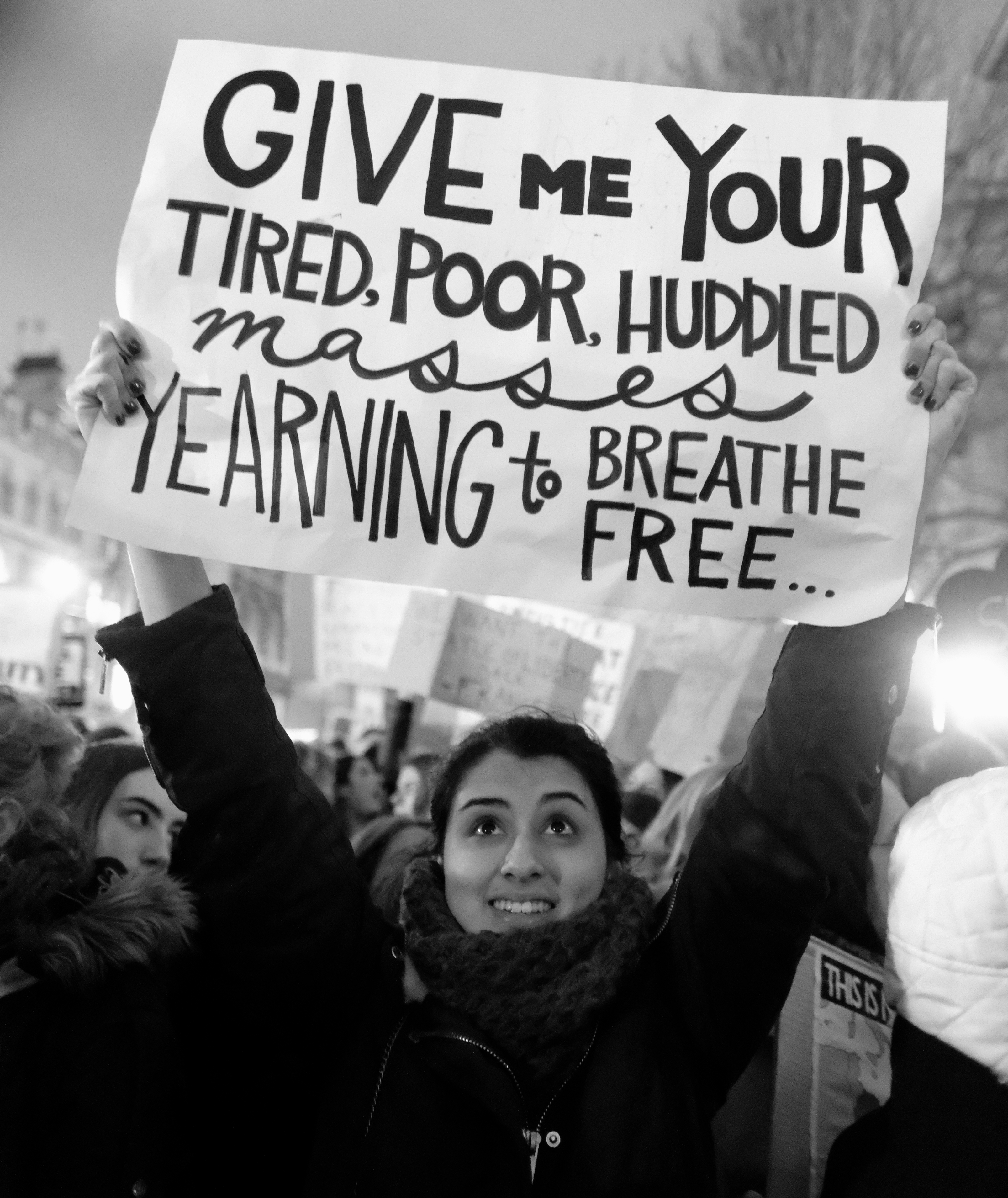 A woman holds a sign quoting the Statue of Liberty at an outdoor protest.