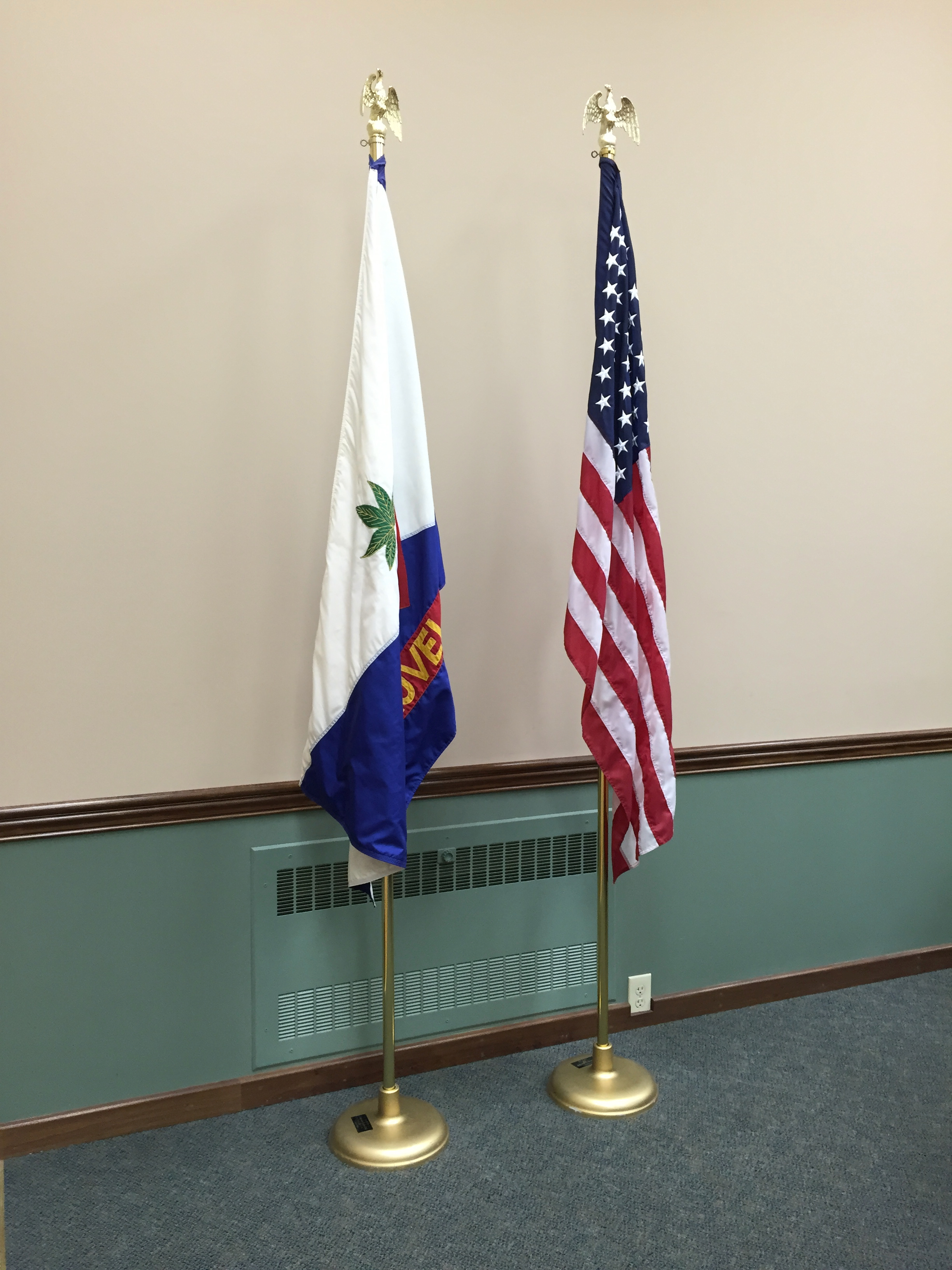 Loveland city flag and U.S. flag on gold poles in a government meeting room.