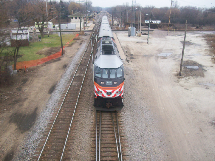 A Metra commuter train travels along railroad tracks through a small Illinois town.