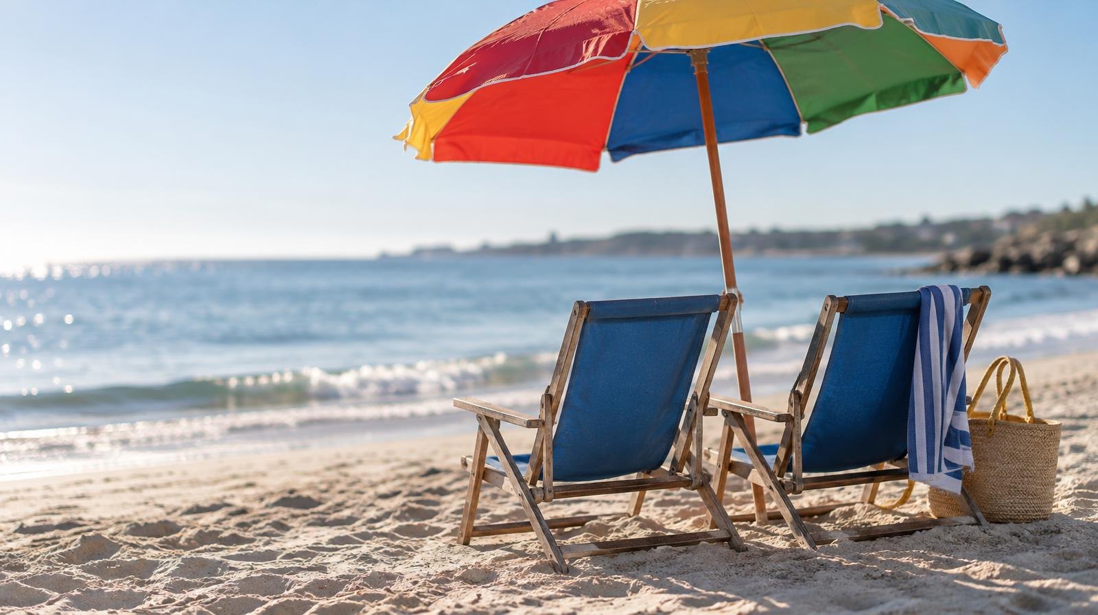 Two empty beach chairs and a colorful umbrella on a sunny sandy beach.