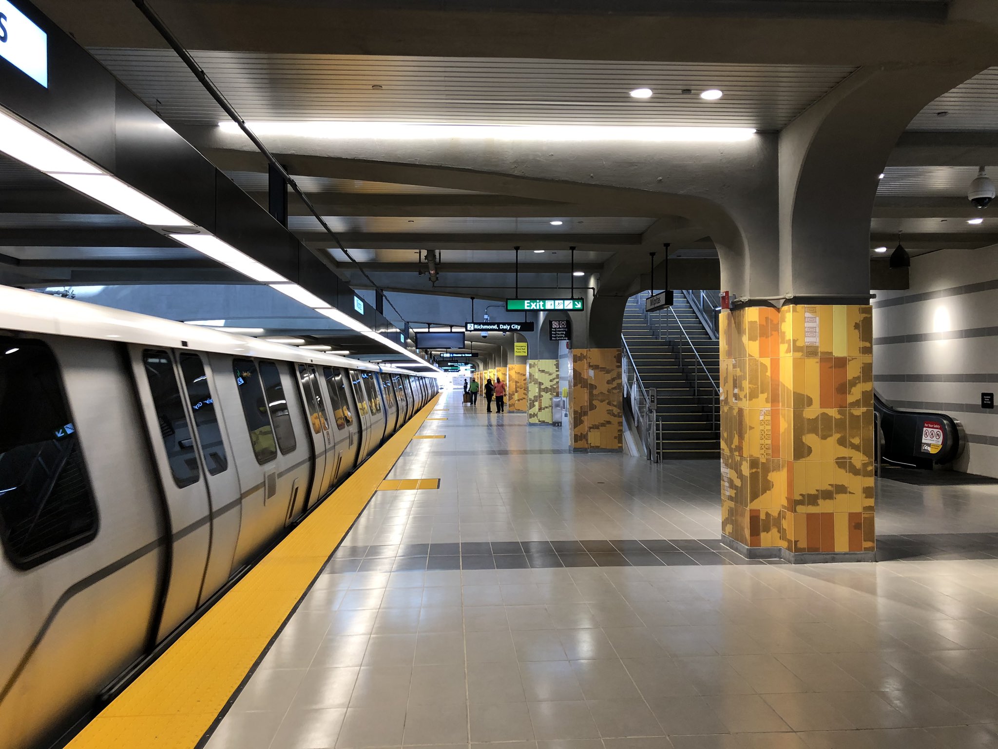 A BART train stopped at a modern station platform with yellow edge markings and decorative columns.