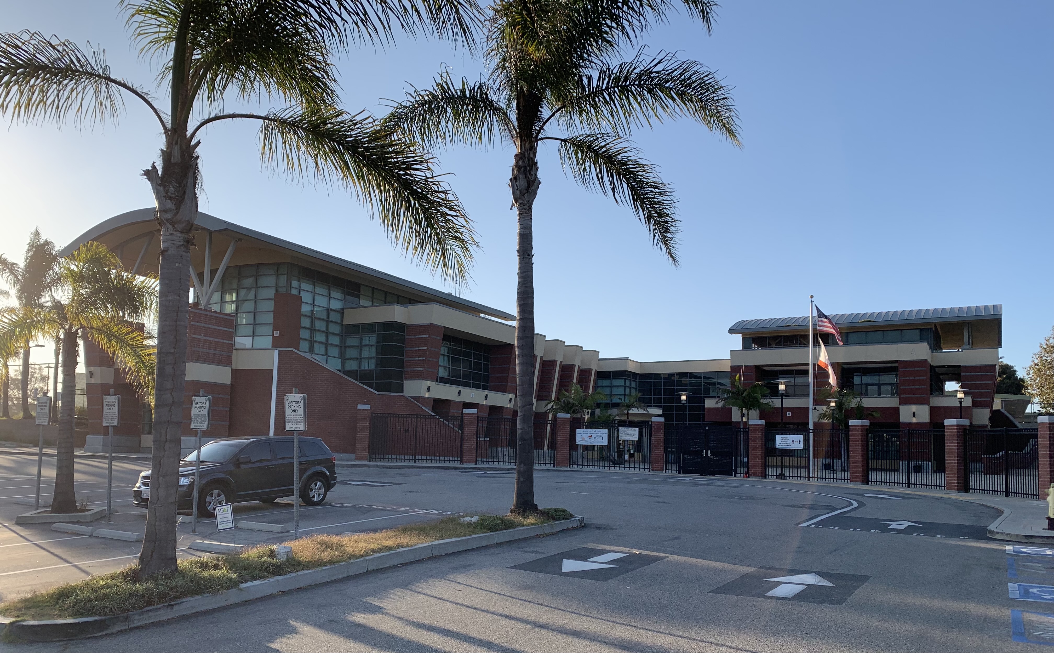 Brick high school building with palm trees and an American flag out front.
