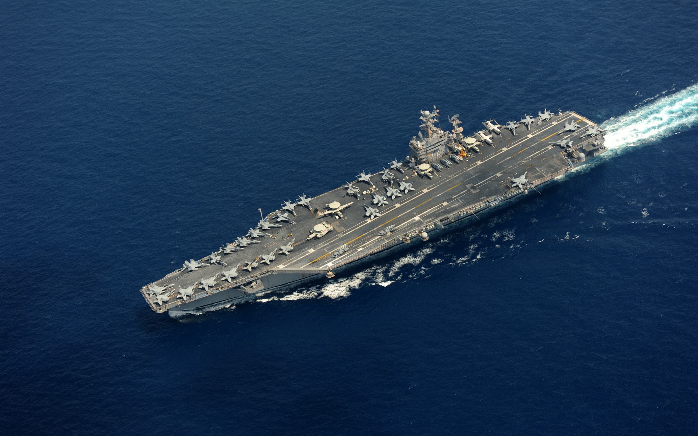 Aerial view of a Nimitz-class aircraft carrier underway in open blue ocean.