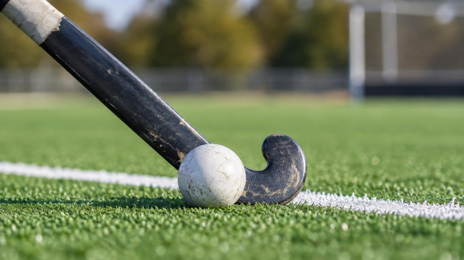 A field hockey stick and ball resting on green artificial turf near a white line.
