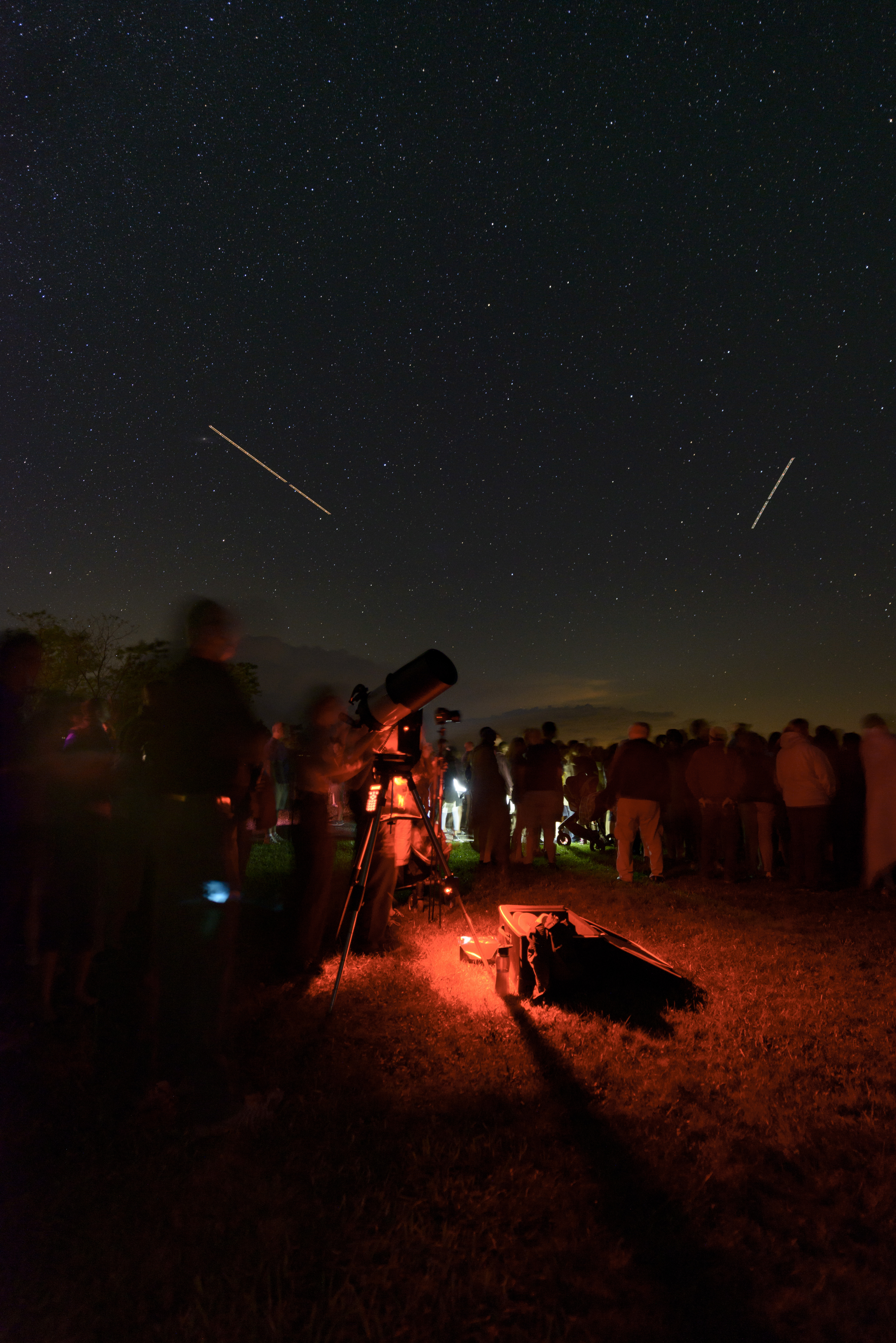 Crowd of people gathered around a telescope under a star-filled night sky.