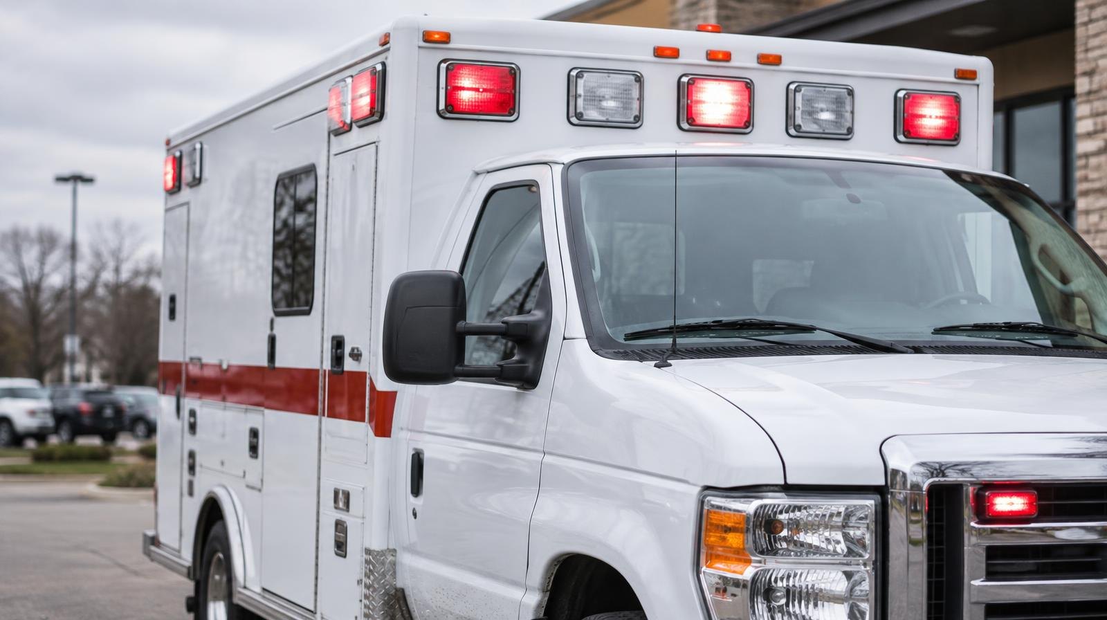 A white ambulance with emergency lights parked outside a building.