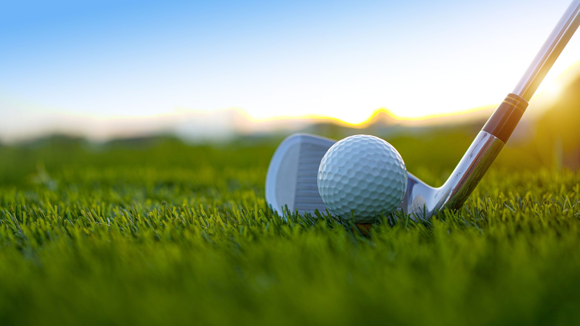 Golf clubs and balls on a green lawn in a golf course with morning sunshine.